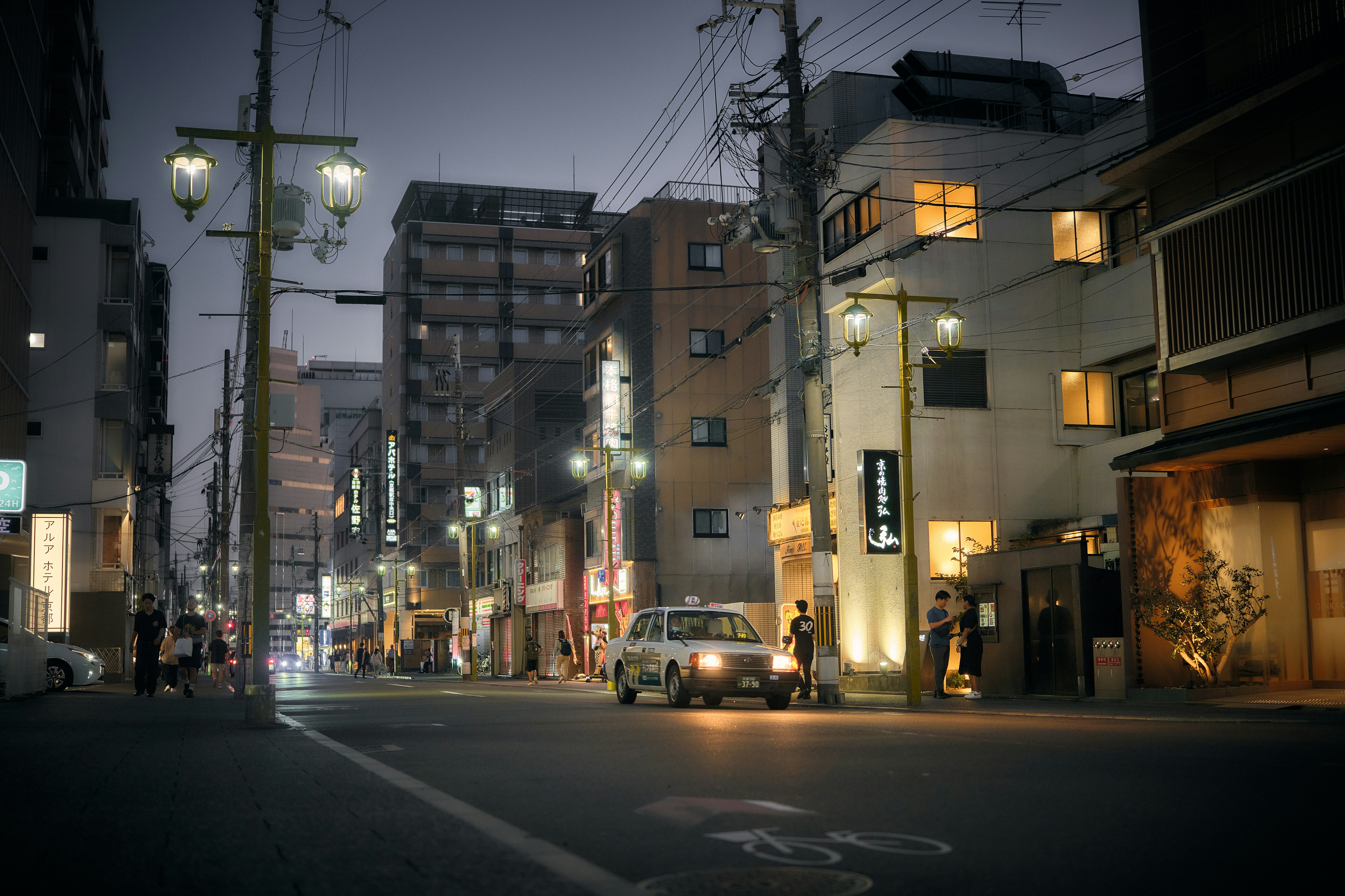 Un taxi blanc dans une rue calme de Kyoto au crépuscule avec des lampadaires lumineux