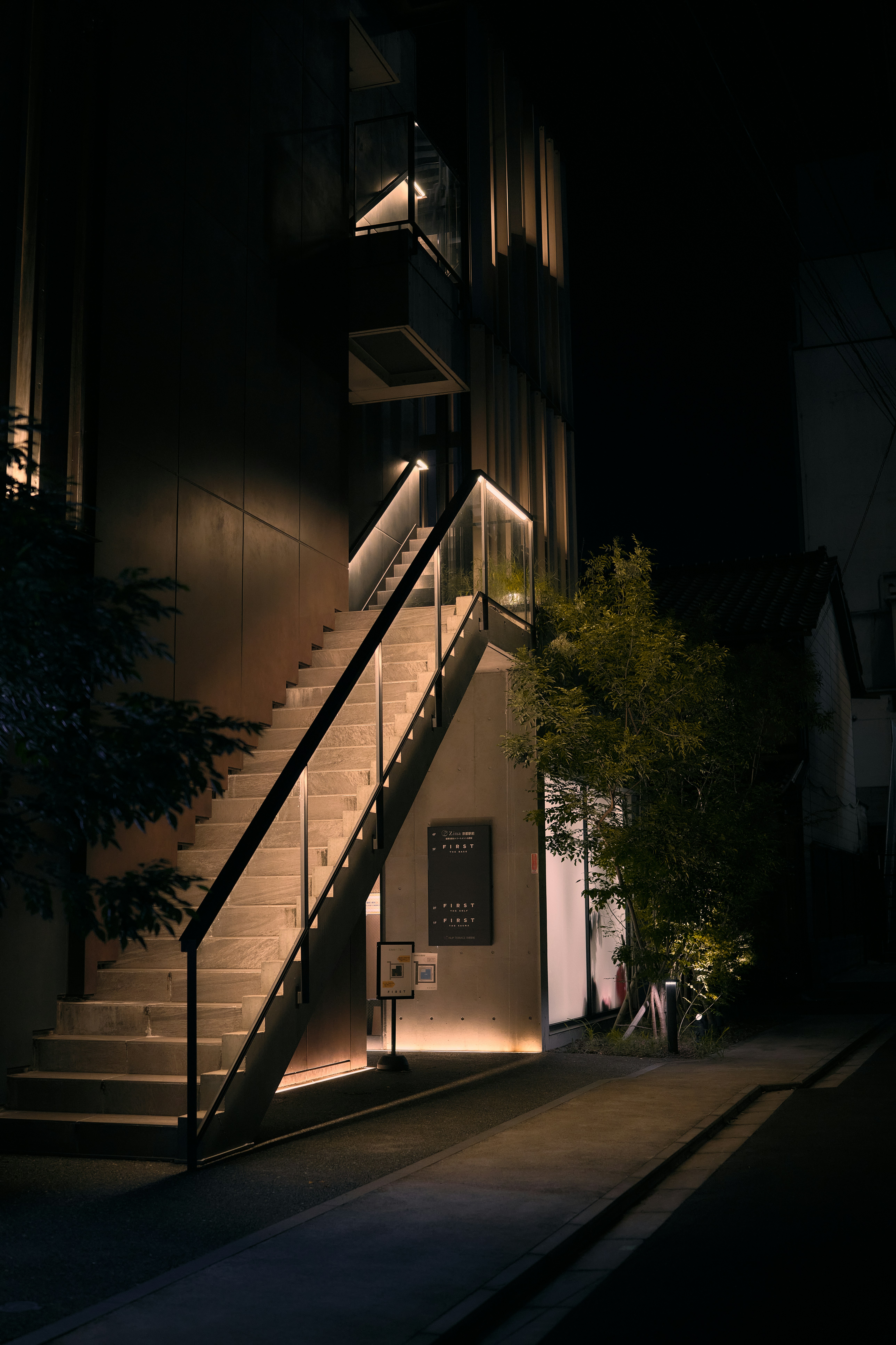 Un escalier extérieur illuminé menant à l’entrée d’un bâtiment moderne la nuit à Kyoto