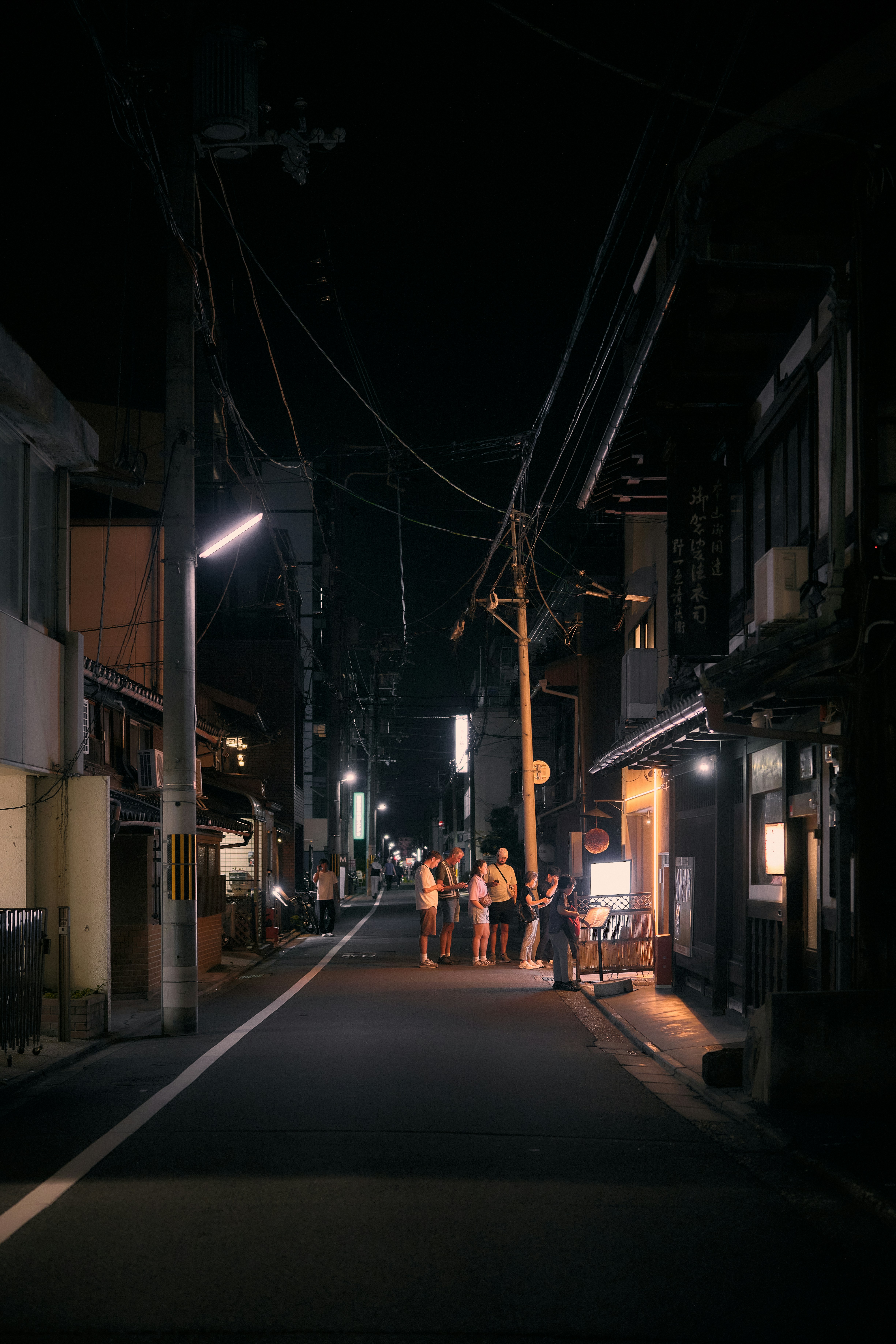 Un groupe de personnes debout dans une rue étroite de Kyoto la nuit