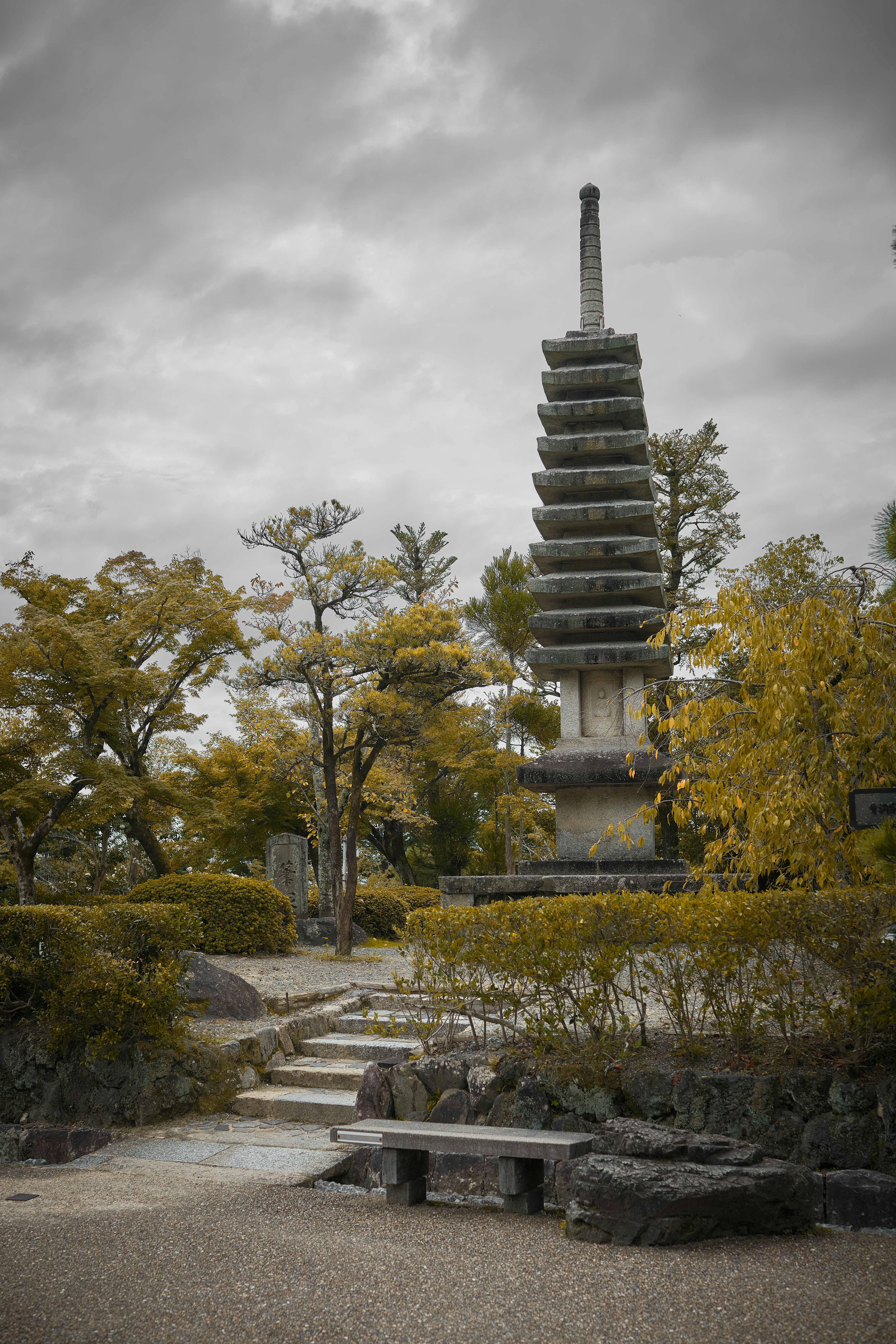 Une pagode de pierre dans un jardin avec des arbres d’automne sous un ciel nuageux à Kyoto