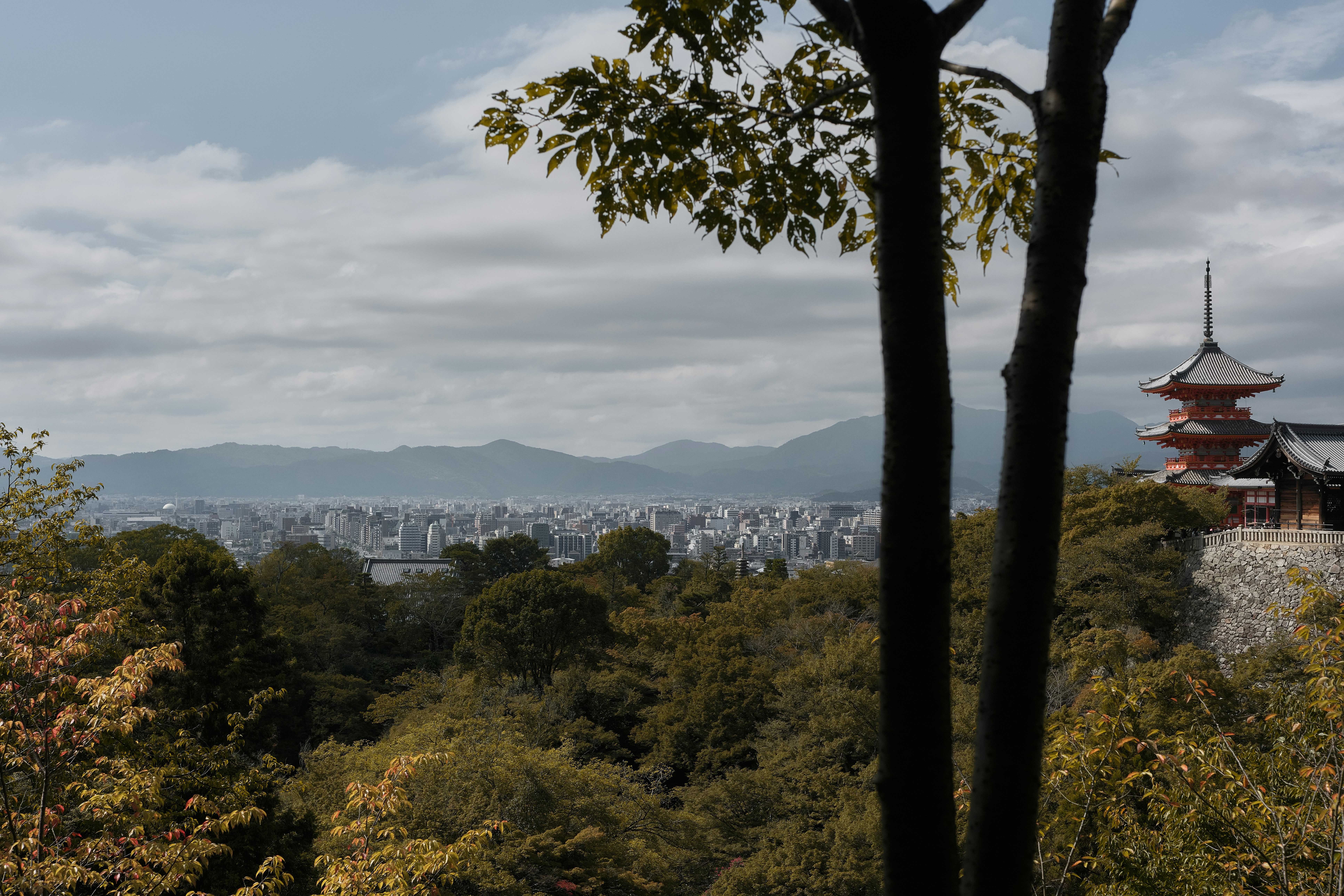 Une pagode surplombant la ville de Kyoto, avec des montagnes lointaines sous un ciel nuageux