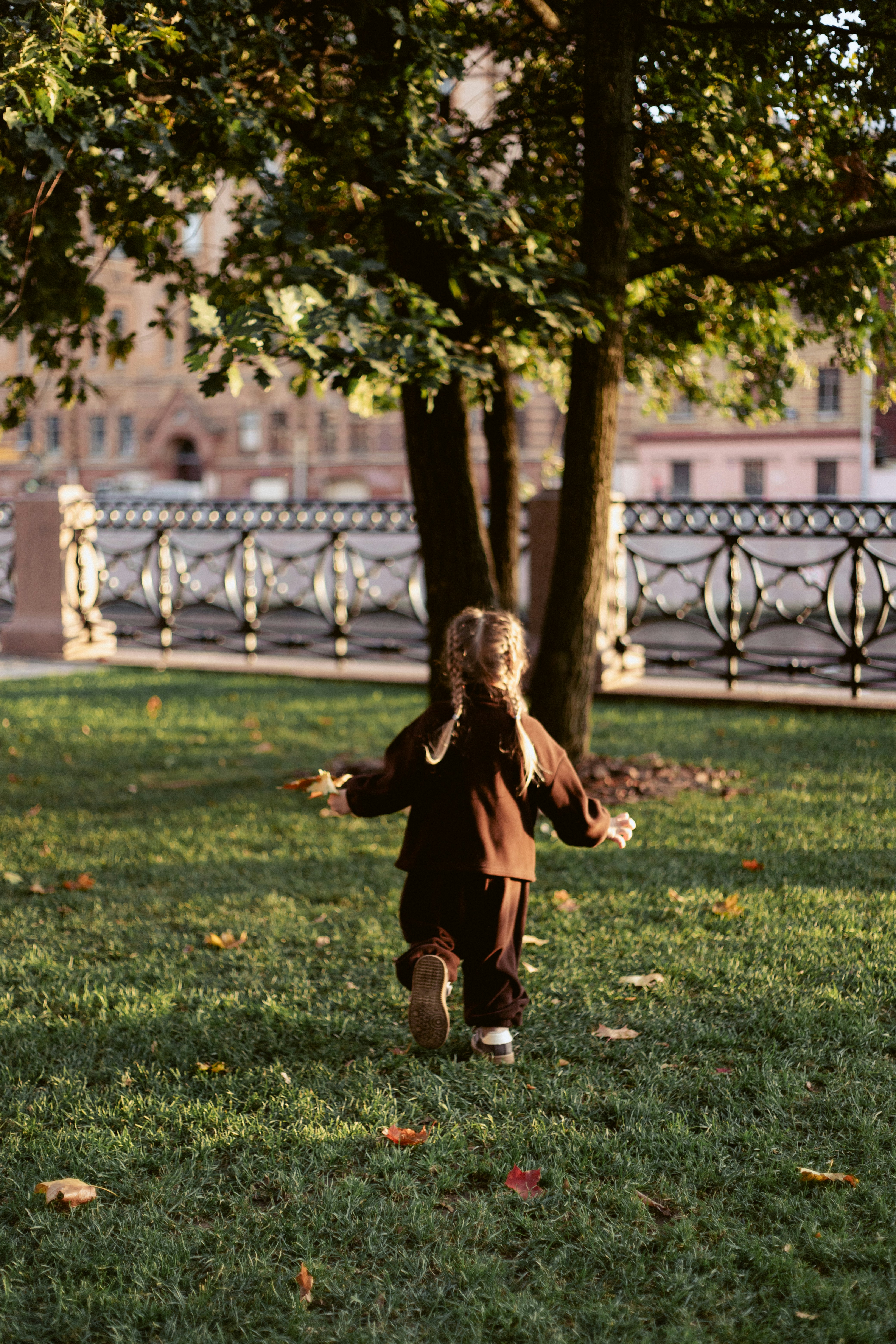 A child with braided hair running across a grassy park in warm light