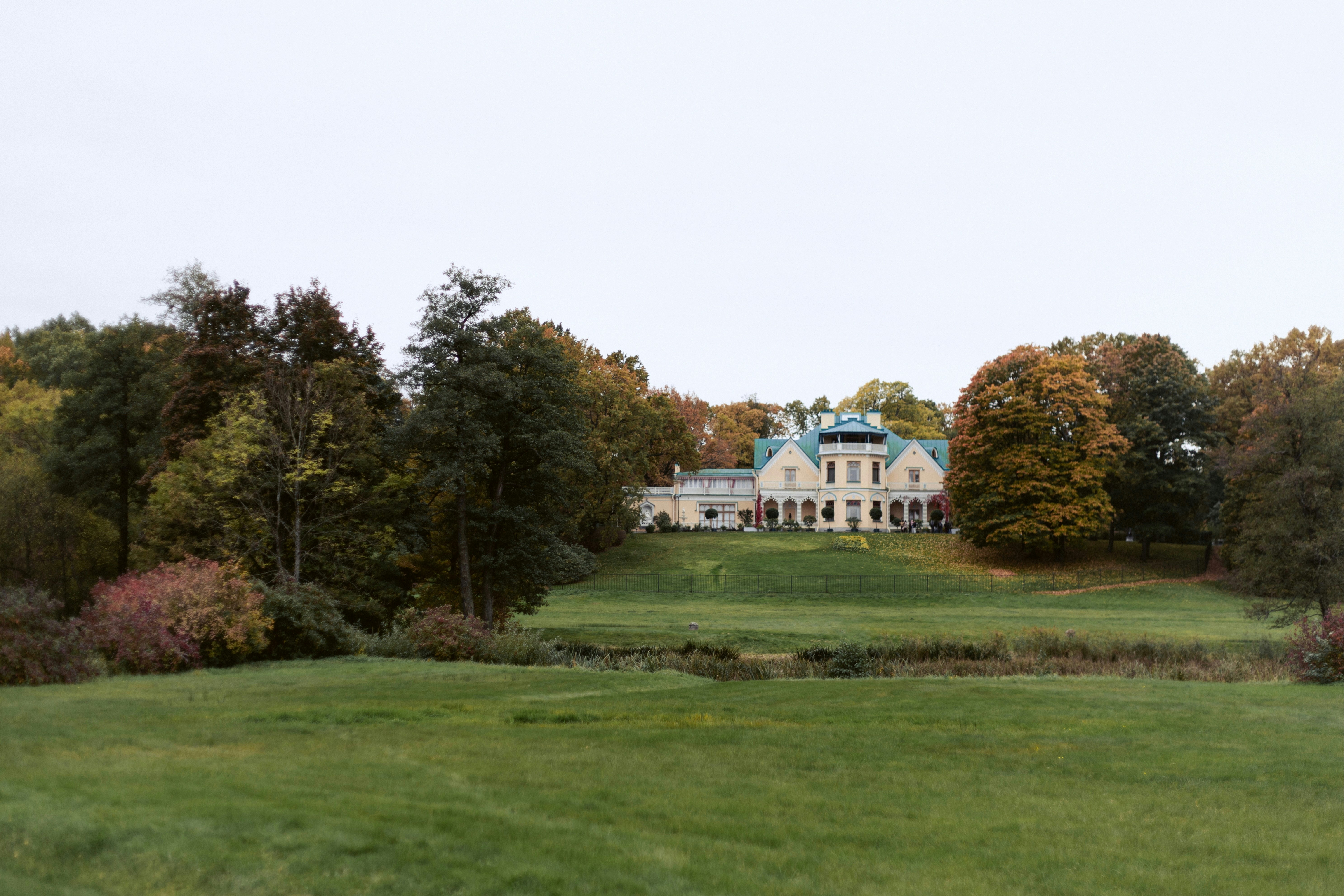 A large yellow manor house with a green roof surrounded by autumn trees