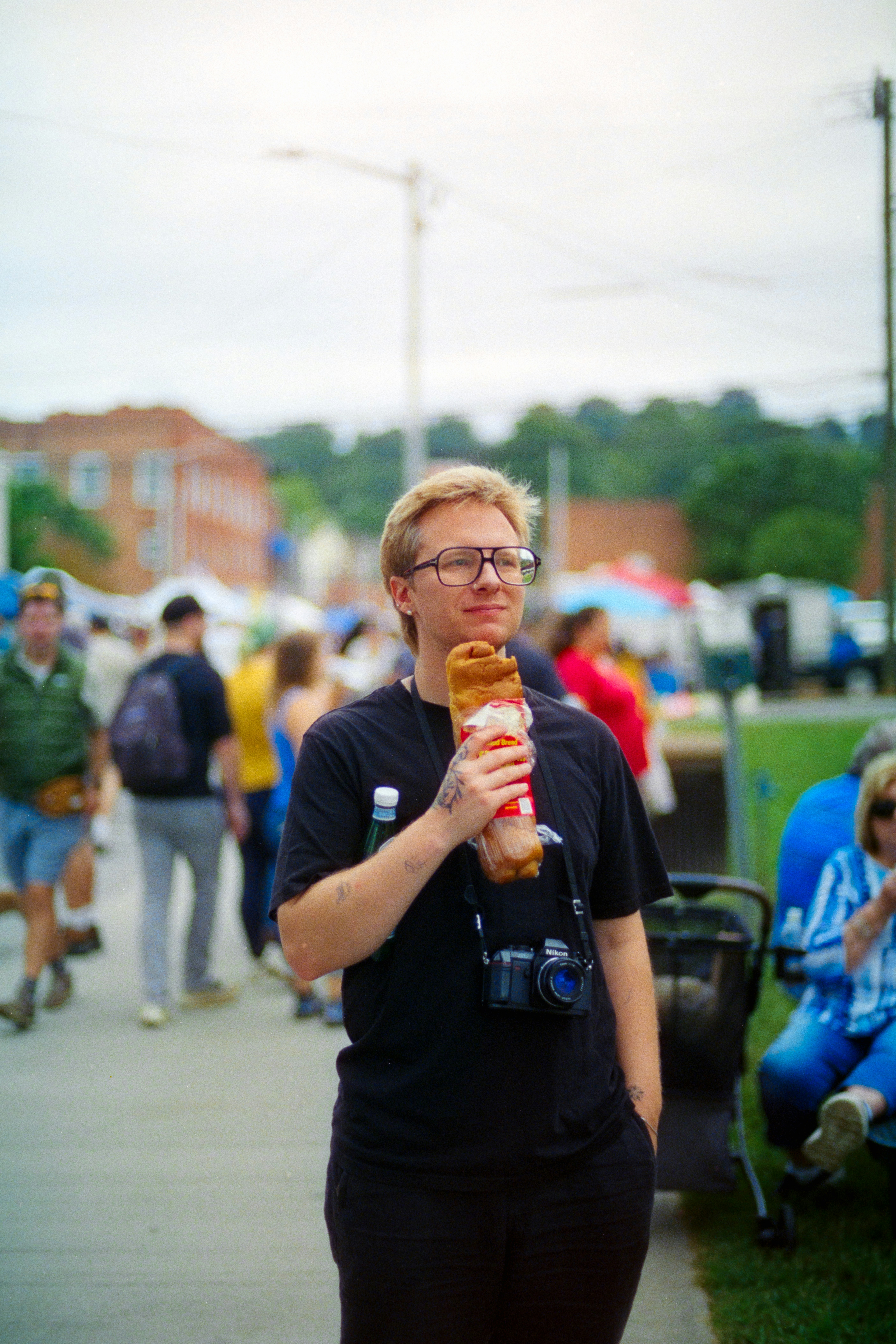 A person with glasses holding a wrapped baguette on a busy outdoor street