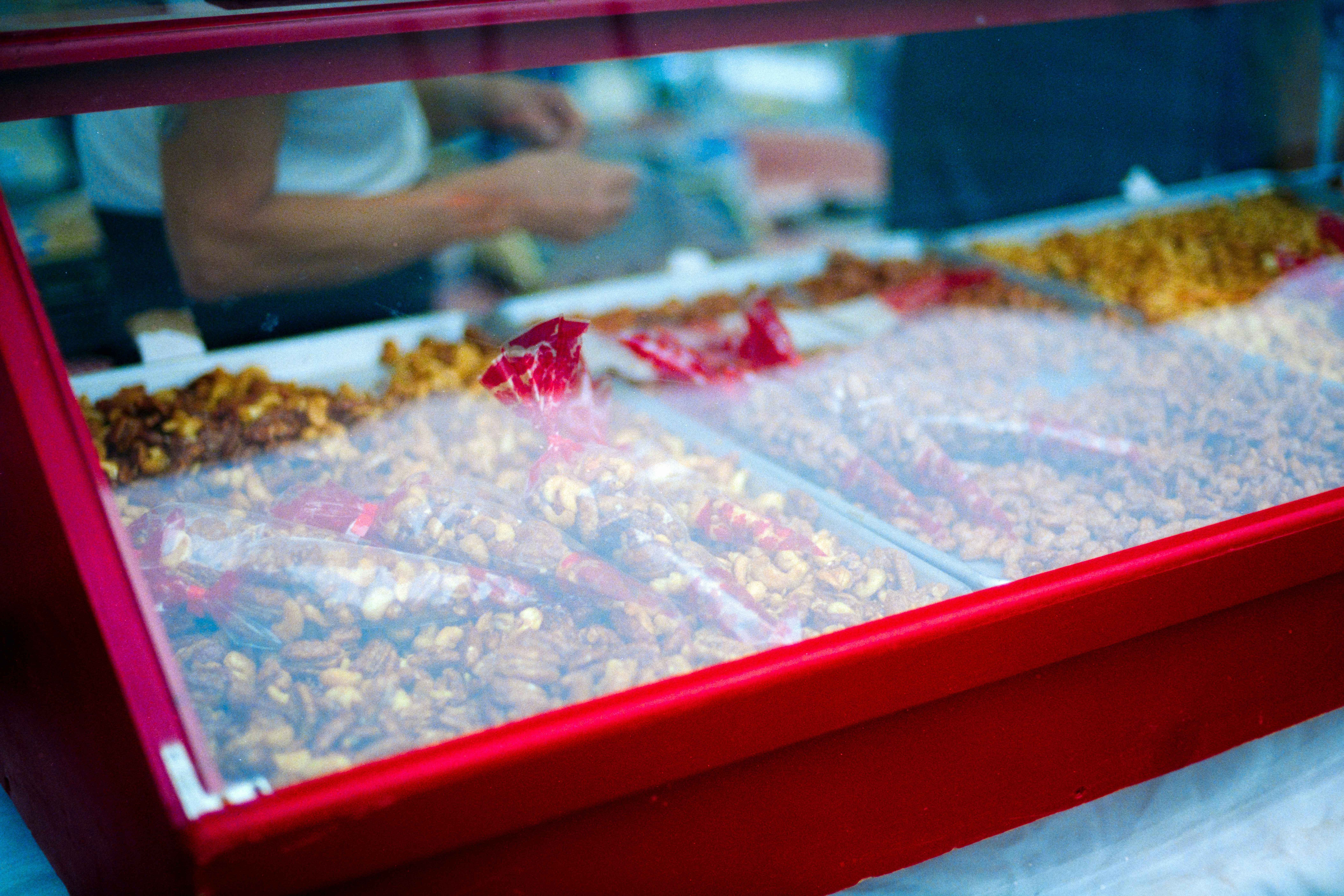 A glass display case filled with roasted nuts in plastic cones at a market stall