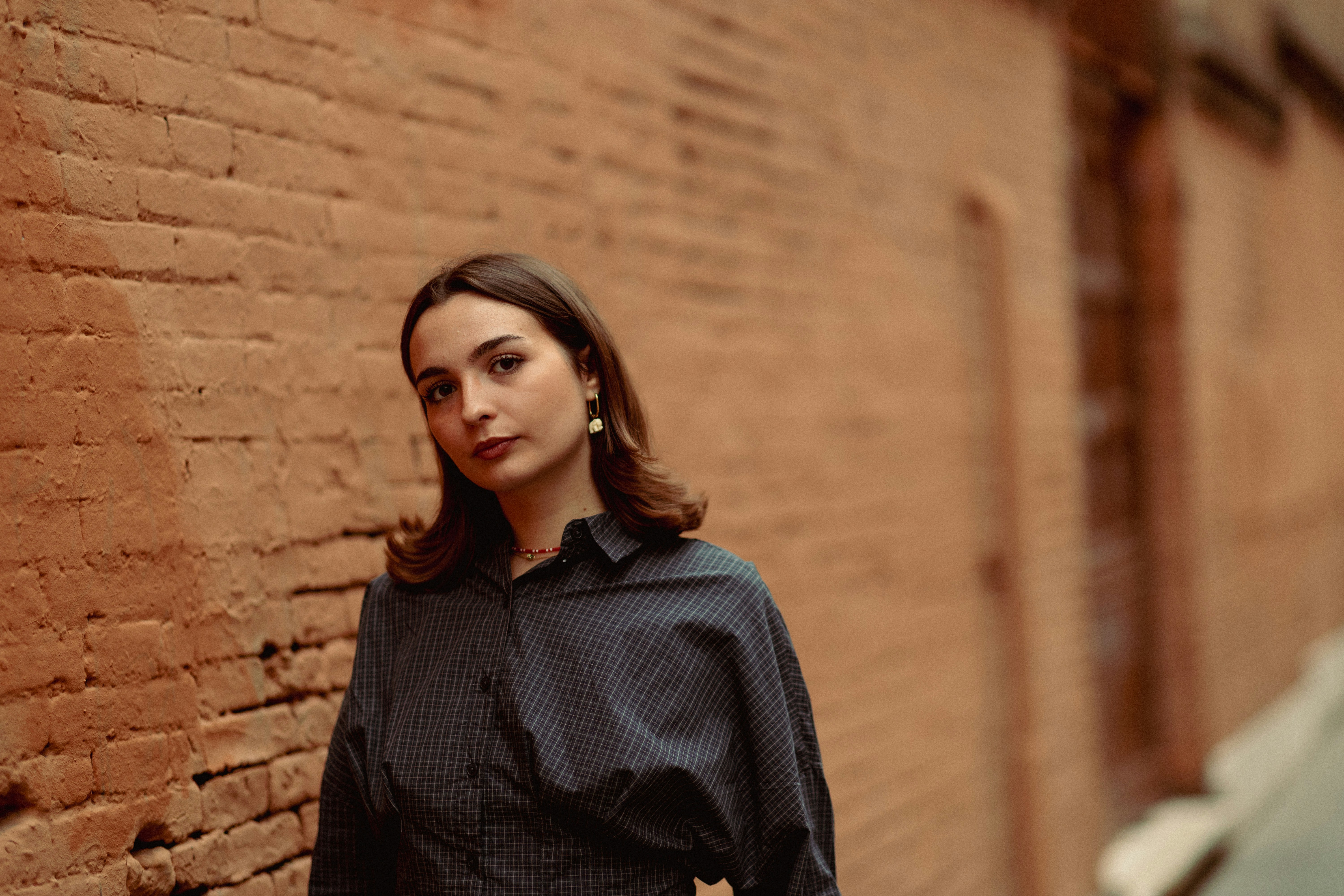 A woman in a dark plaid shirt standing against a textured orange brick wall