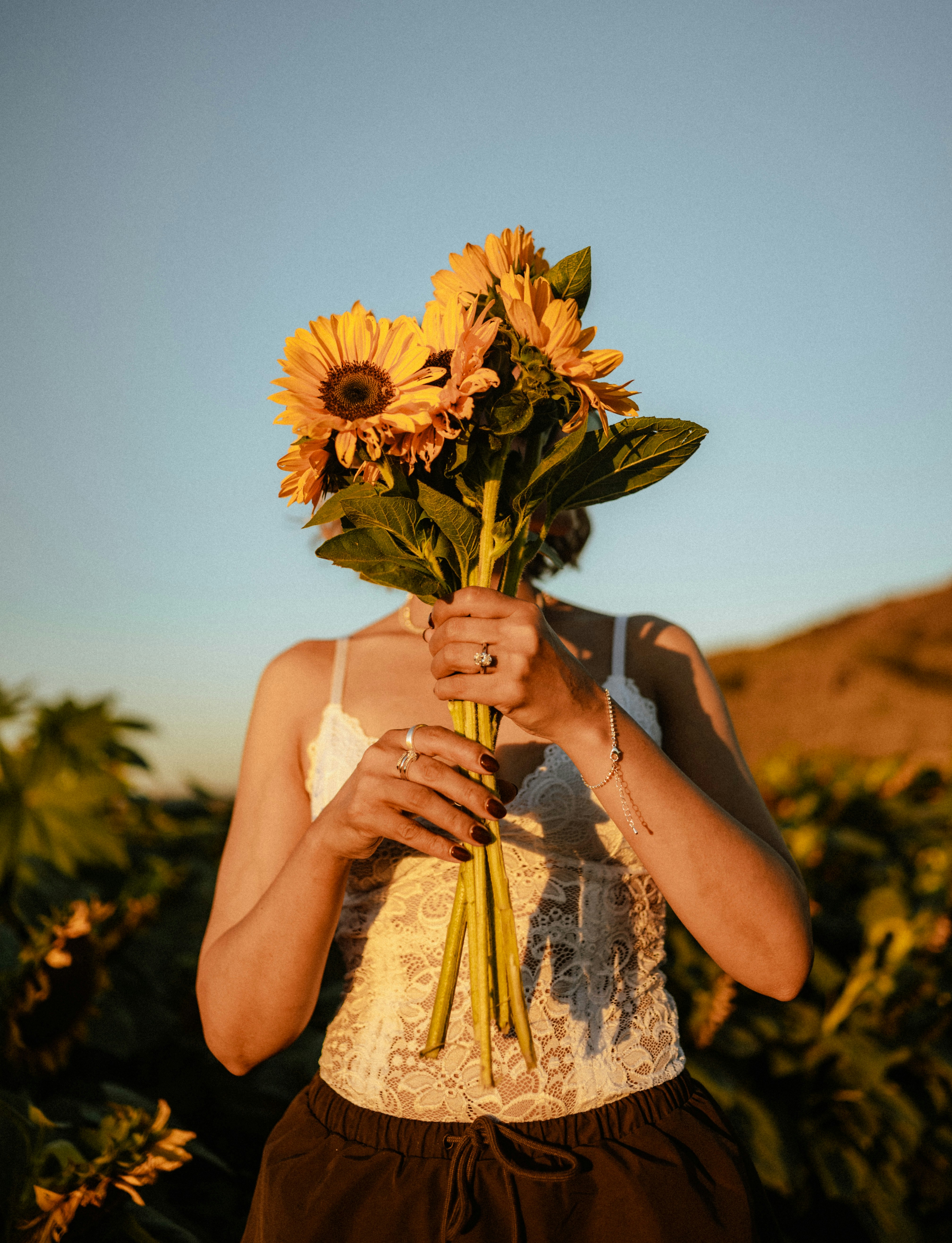 A person holding a bouquet of sunflowers in front of their face in a field