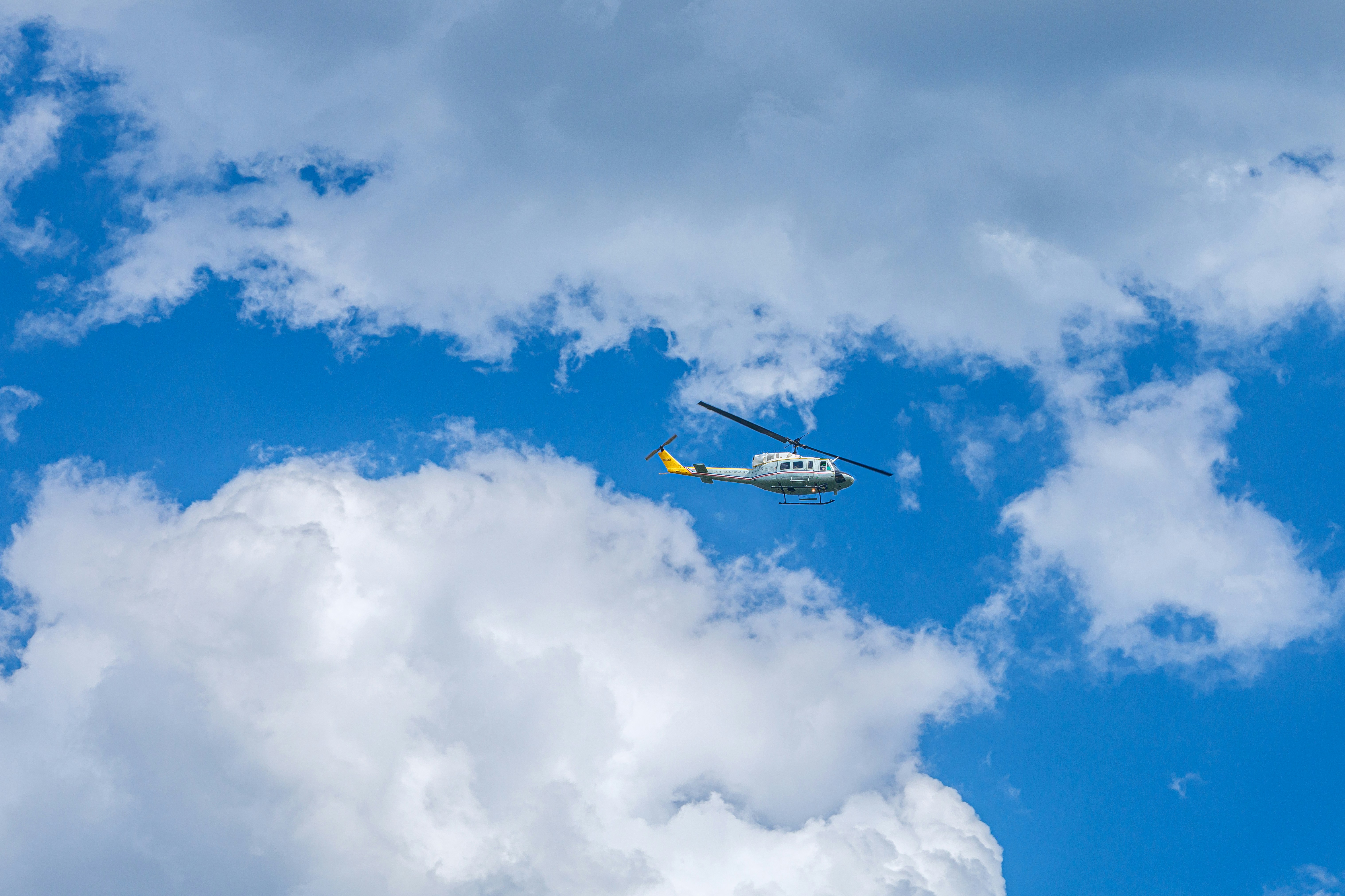 明るい青空を飛び、大きな白い雲が広がる淡い灰色のヘリコプター