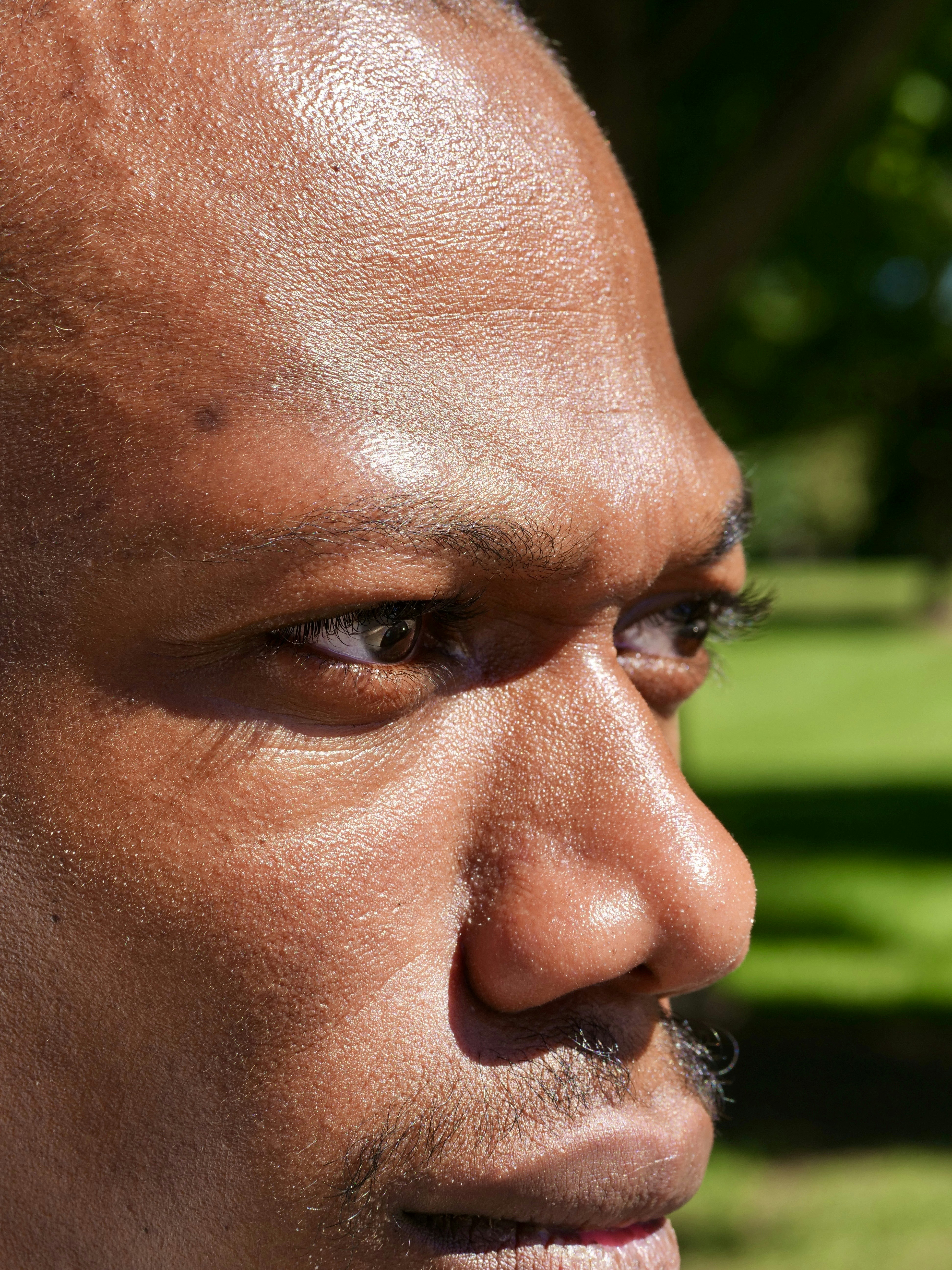 A profile view of an adult man with dark skin in bright sunlight