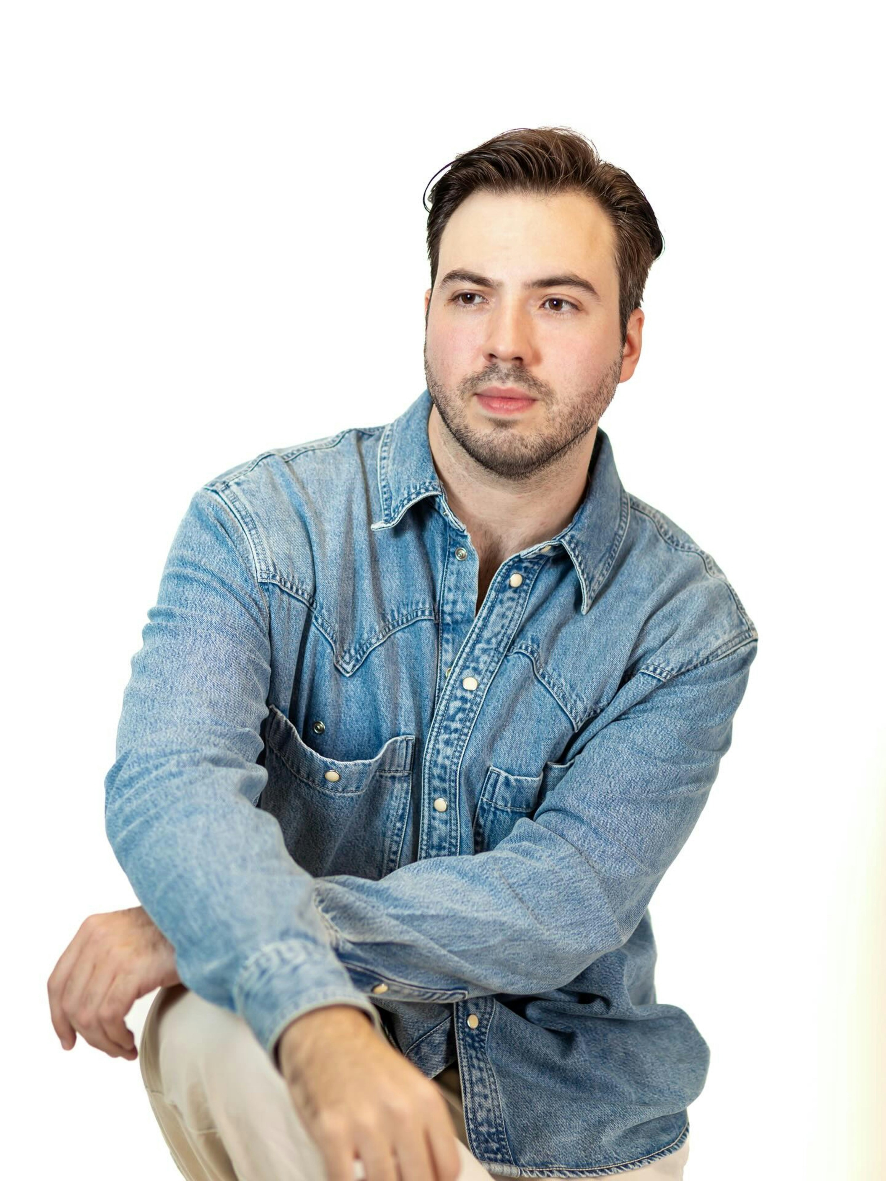 A man with a beard wearing a blue denim shirt against a white background