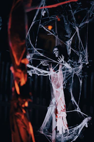 A skeleton decoration draped in artificial spider webs hanging from a tree at night