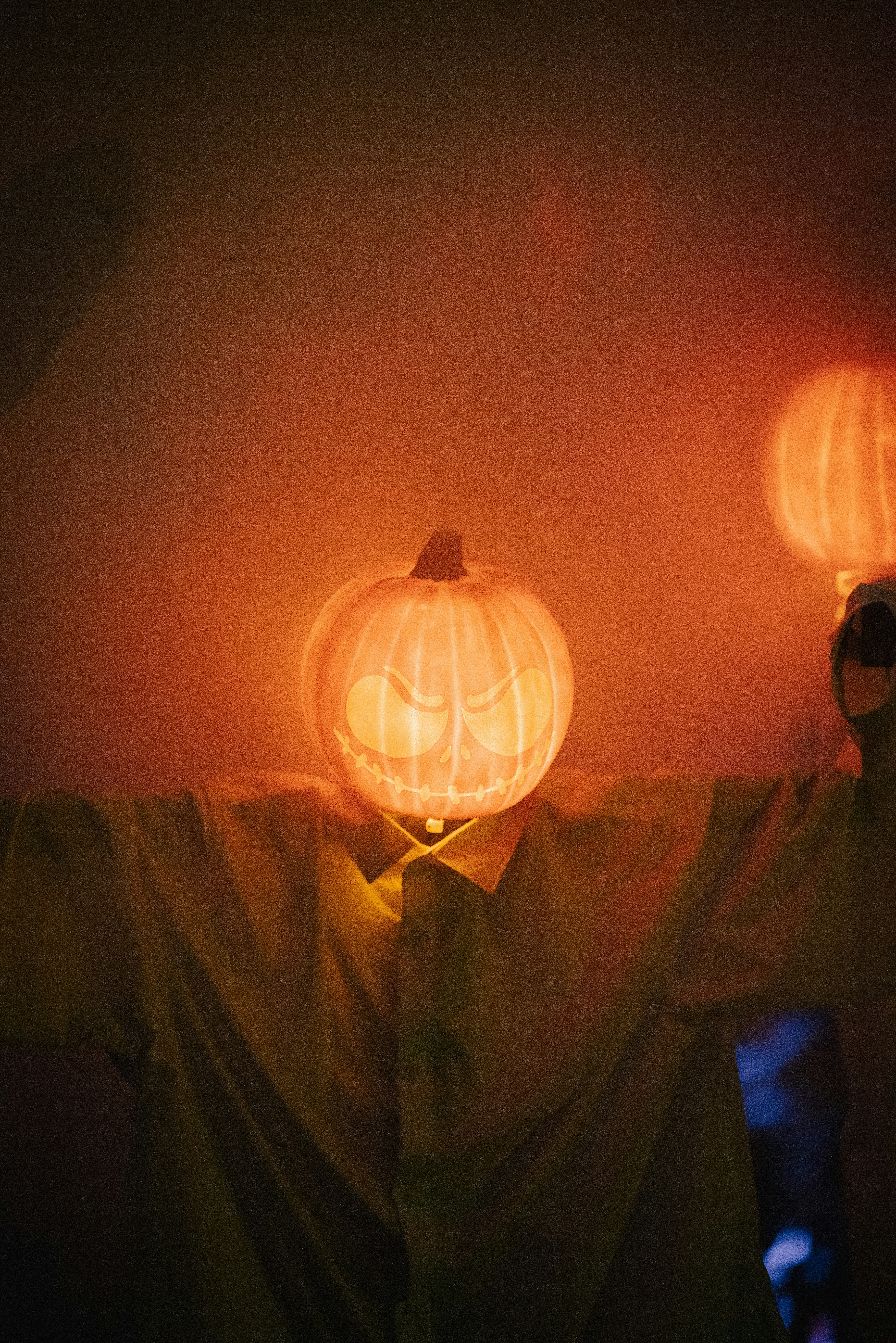 A person wearing a glowing jack-o'-lantern mask with a carved face in a dimly lit room