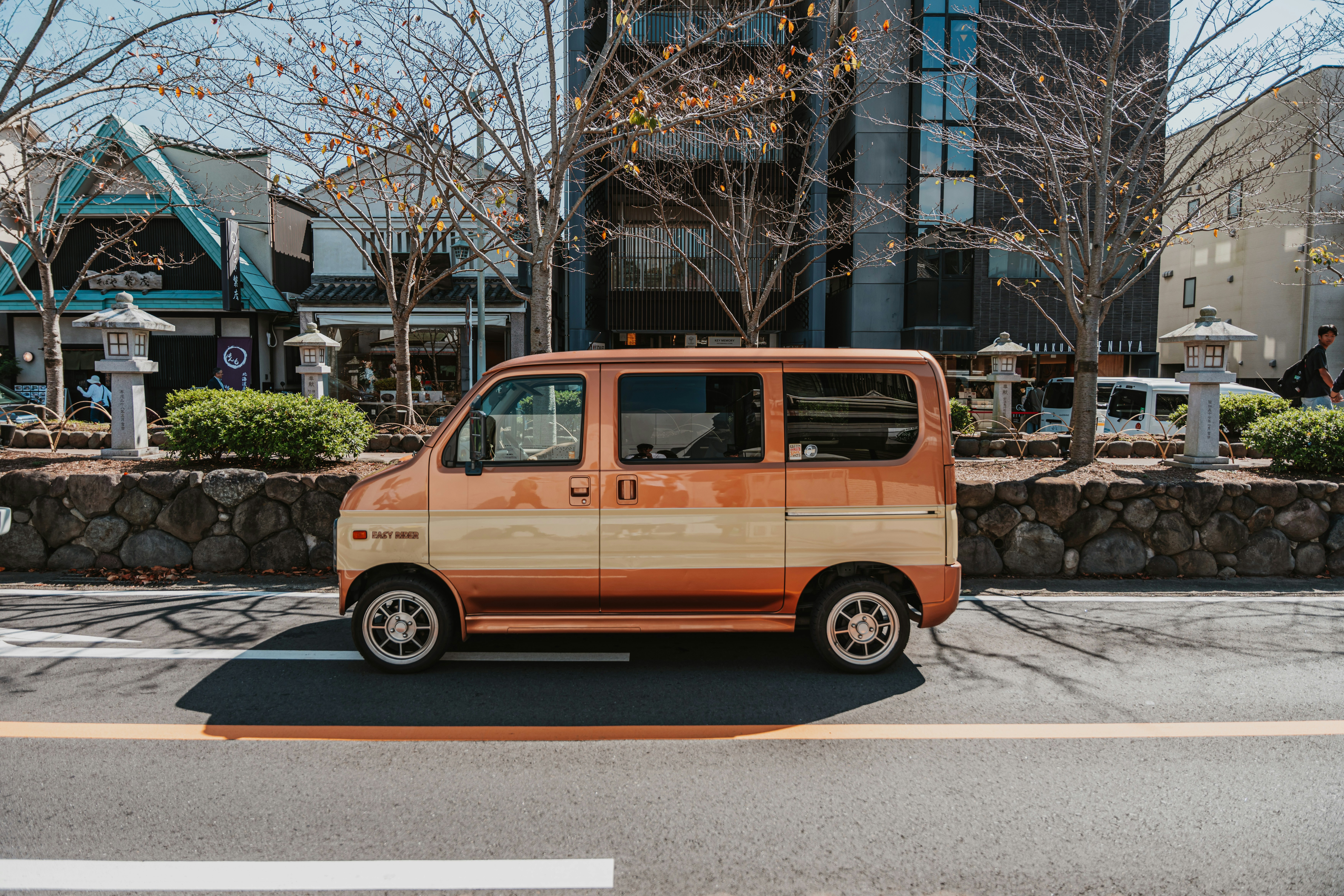 A two-tone copper and cream van parked on a street in Japan with stone lanterns