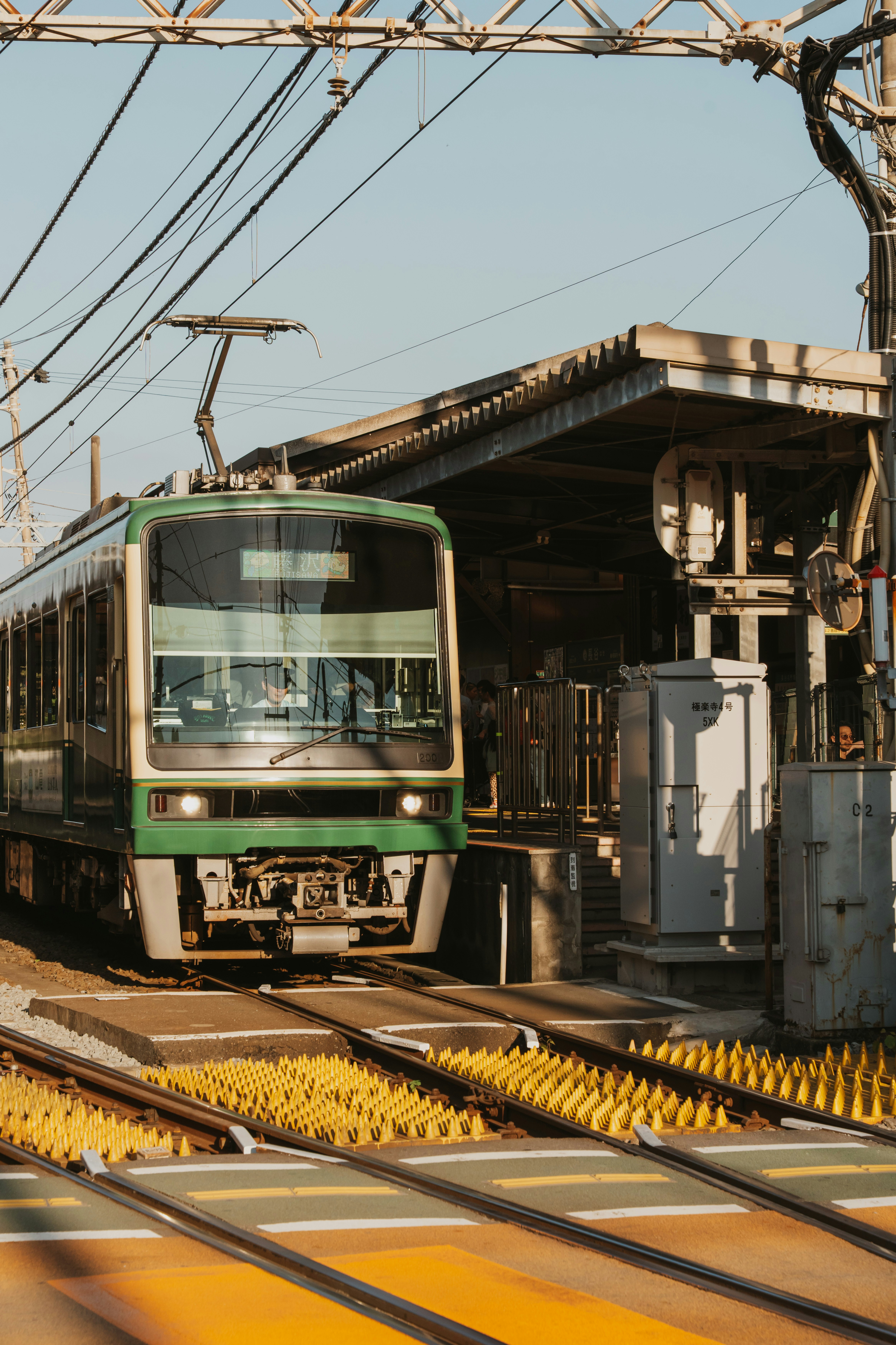 A green and cream commuter train arriving at a station platform in Japan