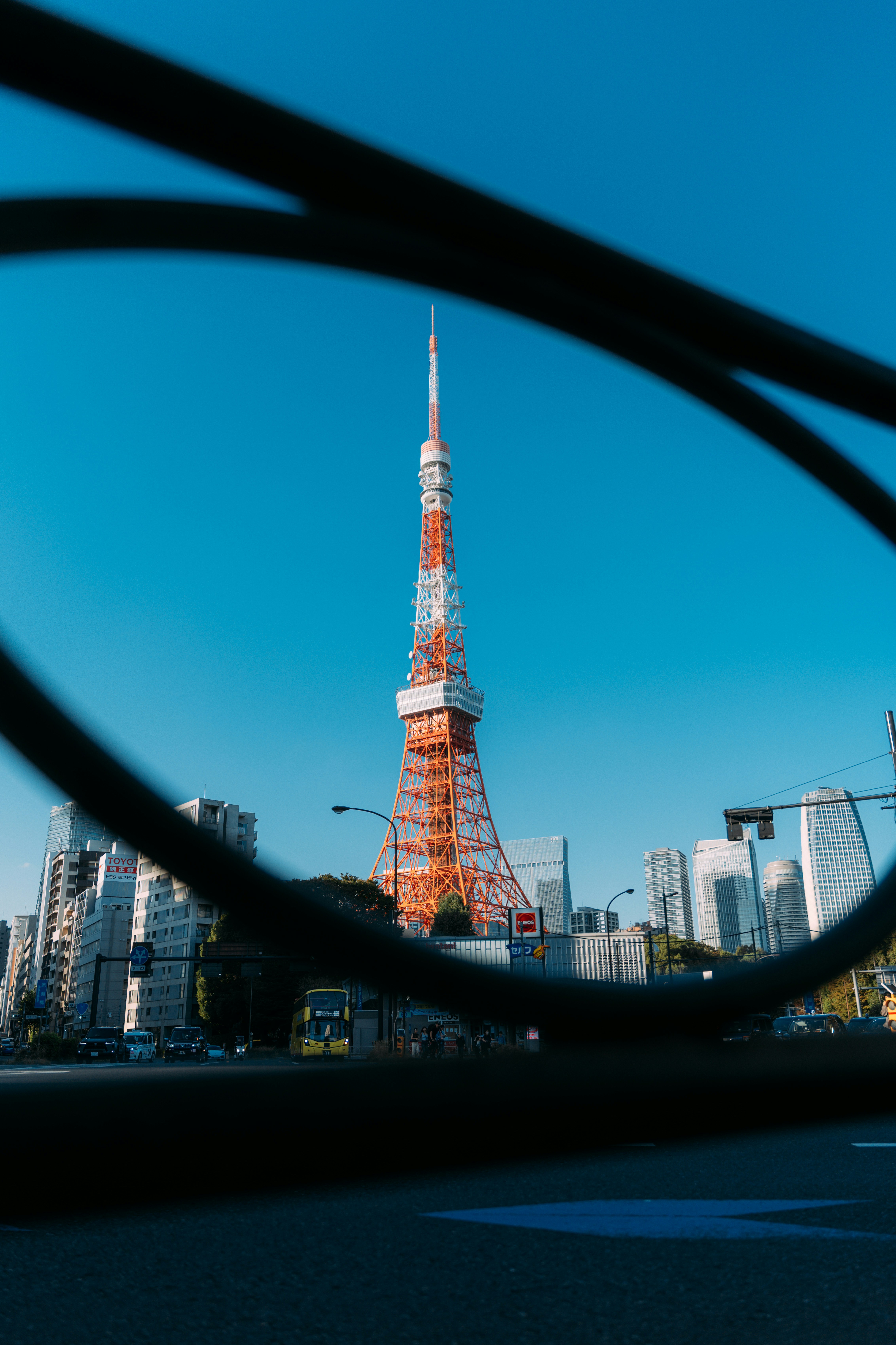 Tokyo Tower framed by a dark curved structure against a clear blue sky