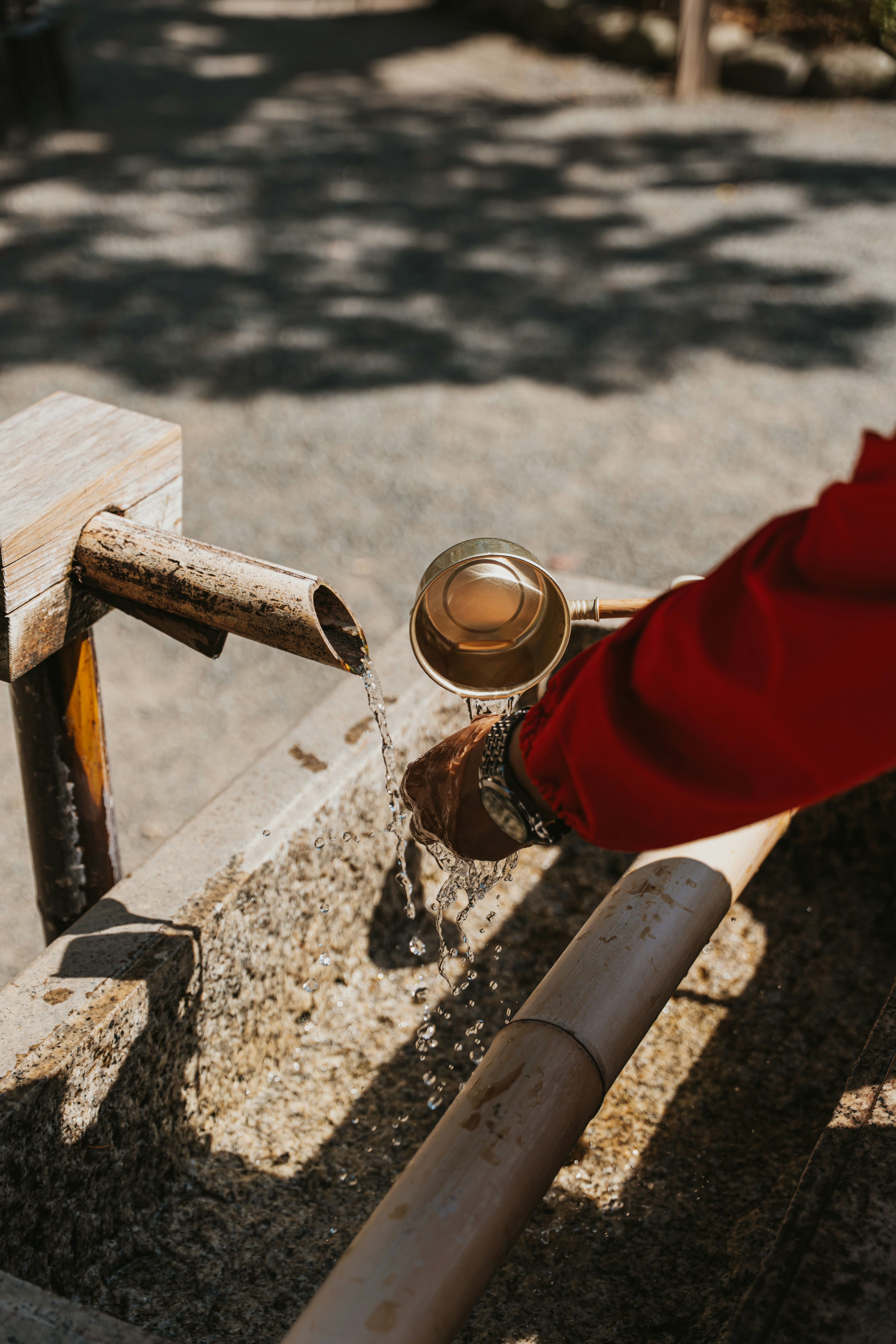 A person in a red sleeve using a bamboo ladle to catch water from a spout