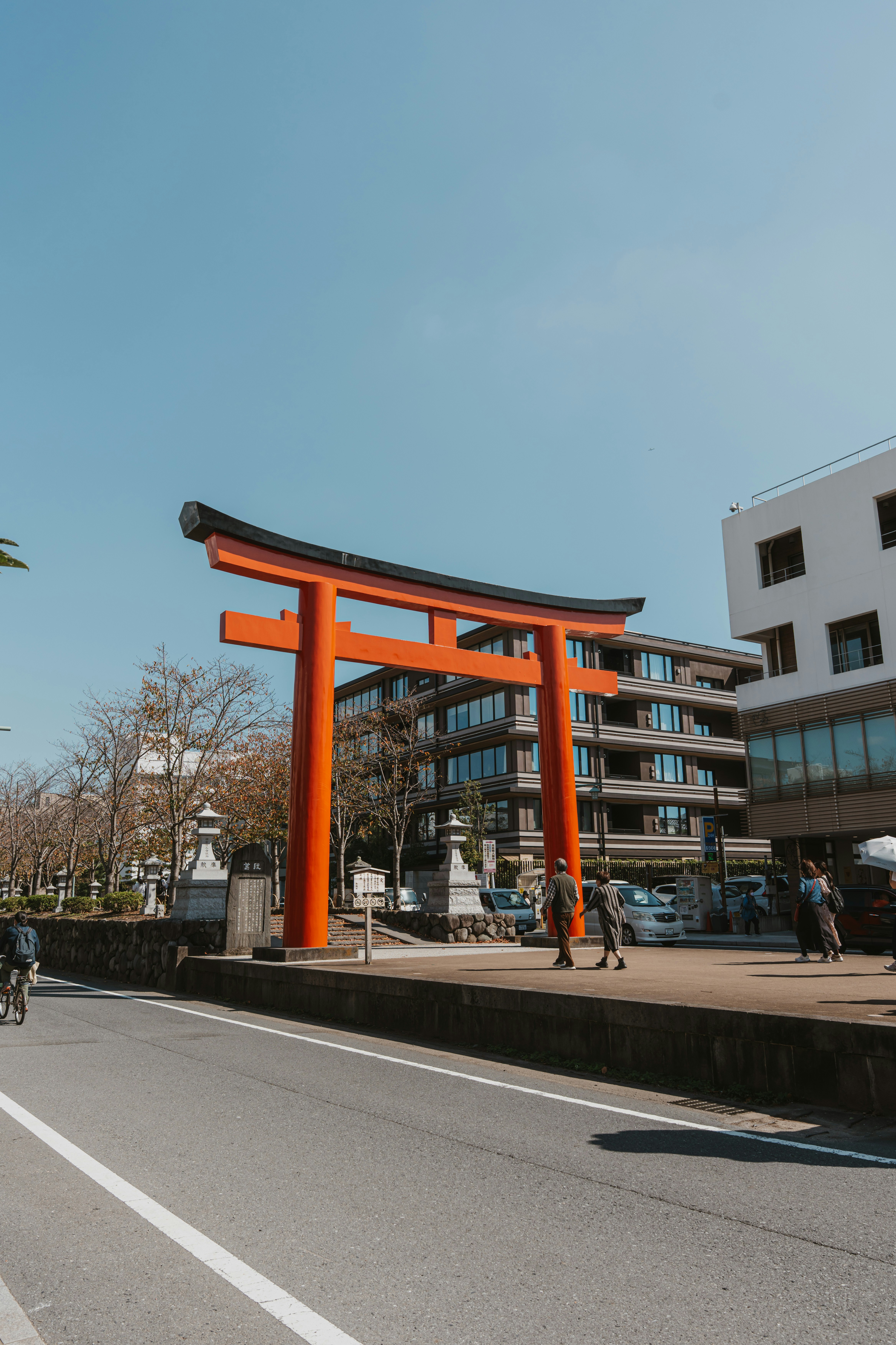A large orange torii gate standing on a paved plaza in a Japanese city