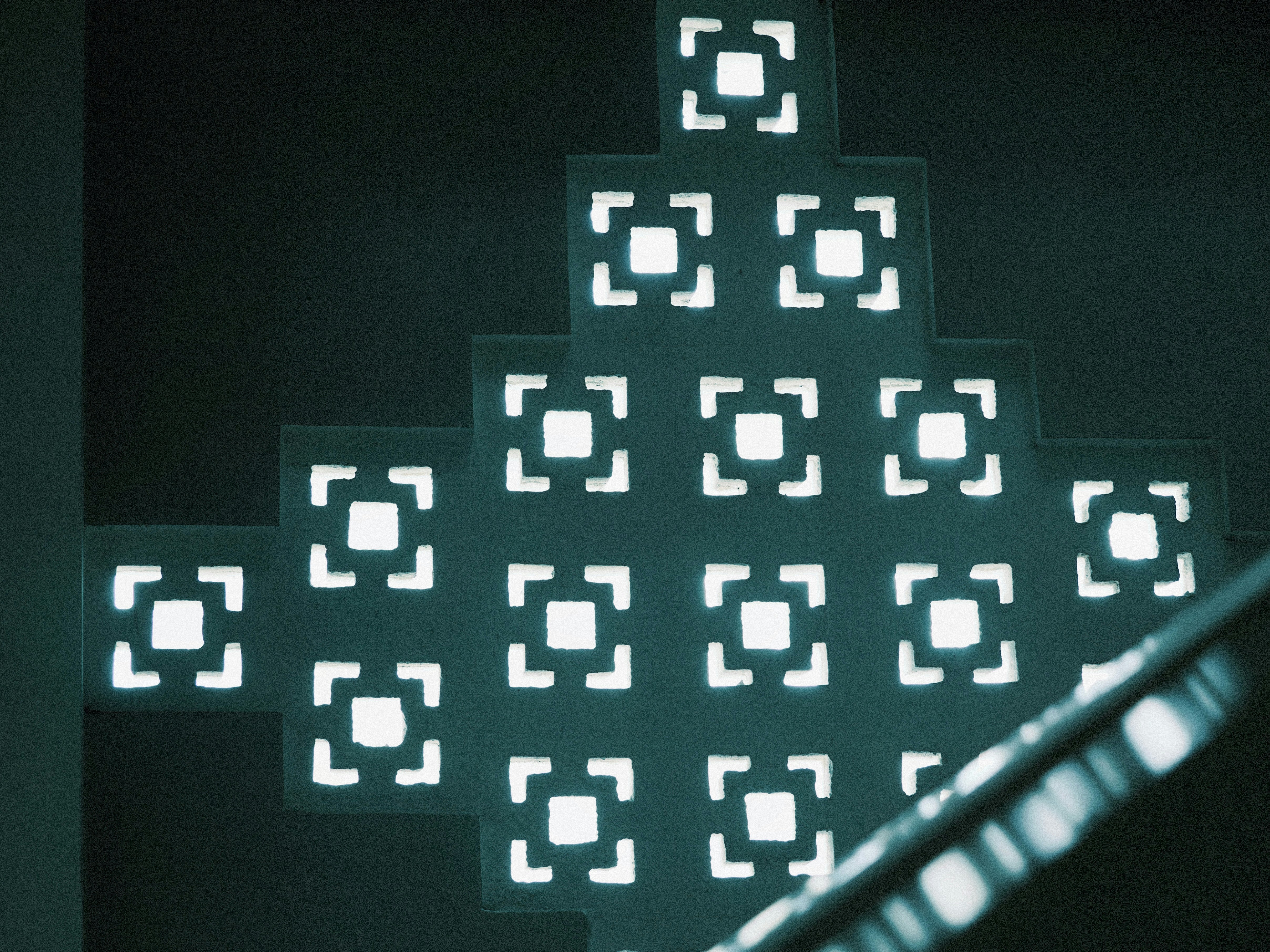 A geometric wall with square cutouts glowing with bright light in a dark room