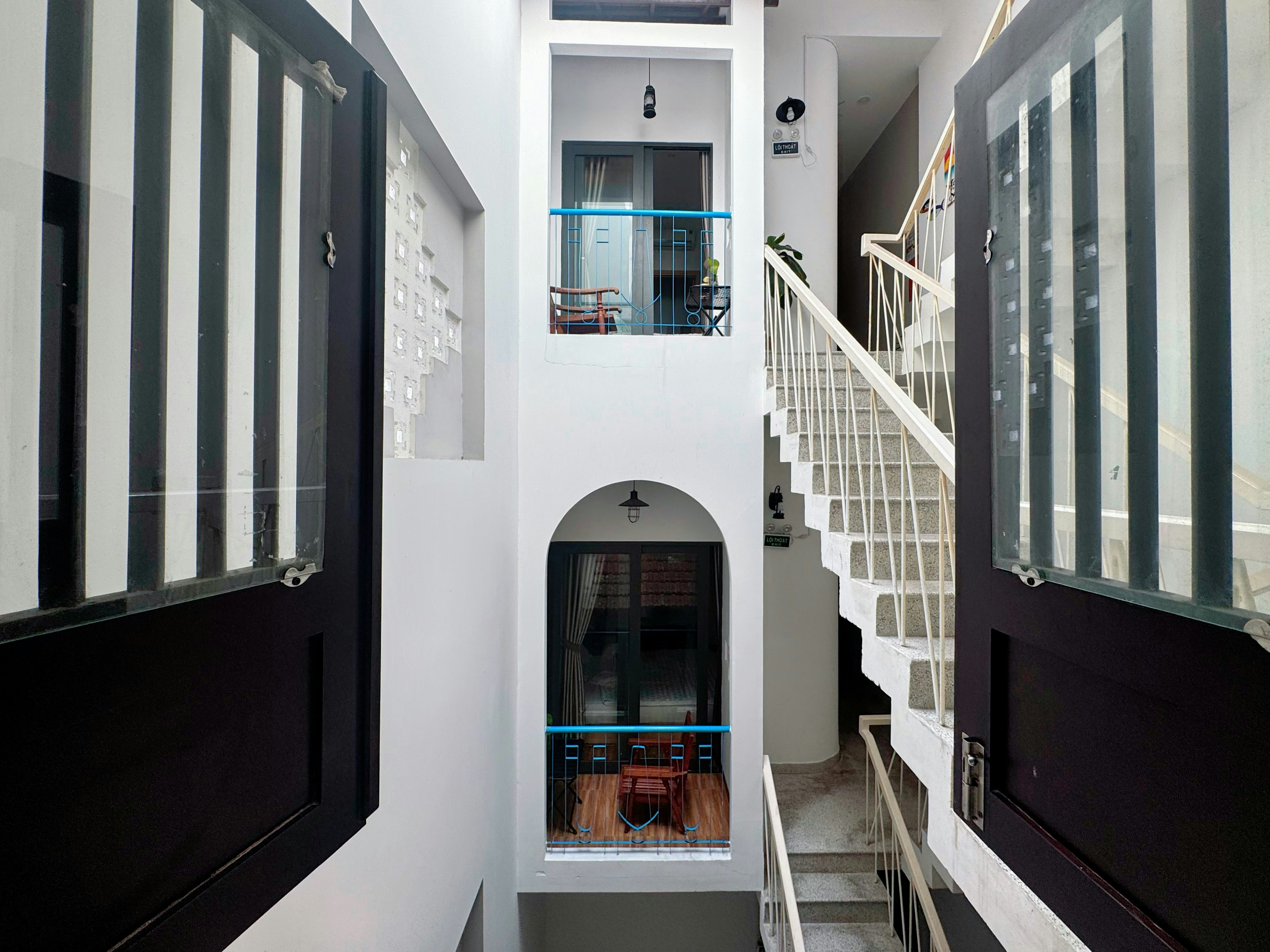 A white stairwell with arched doorways and balconies overlooking a central vertical atrium