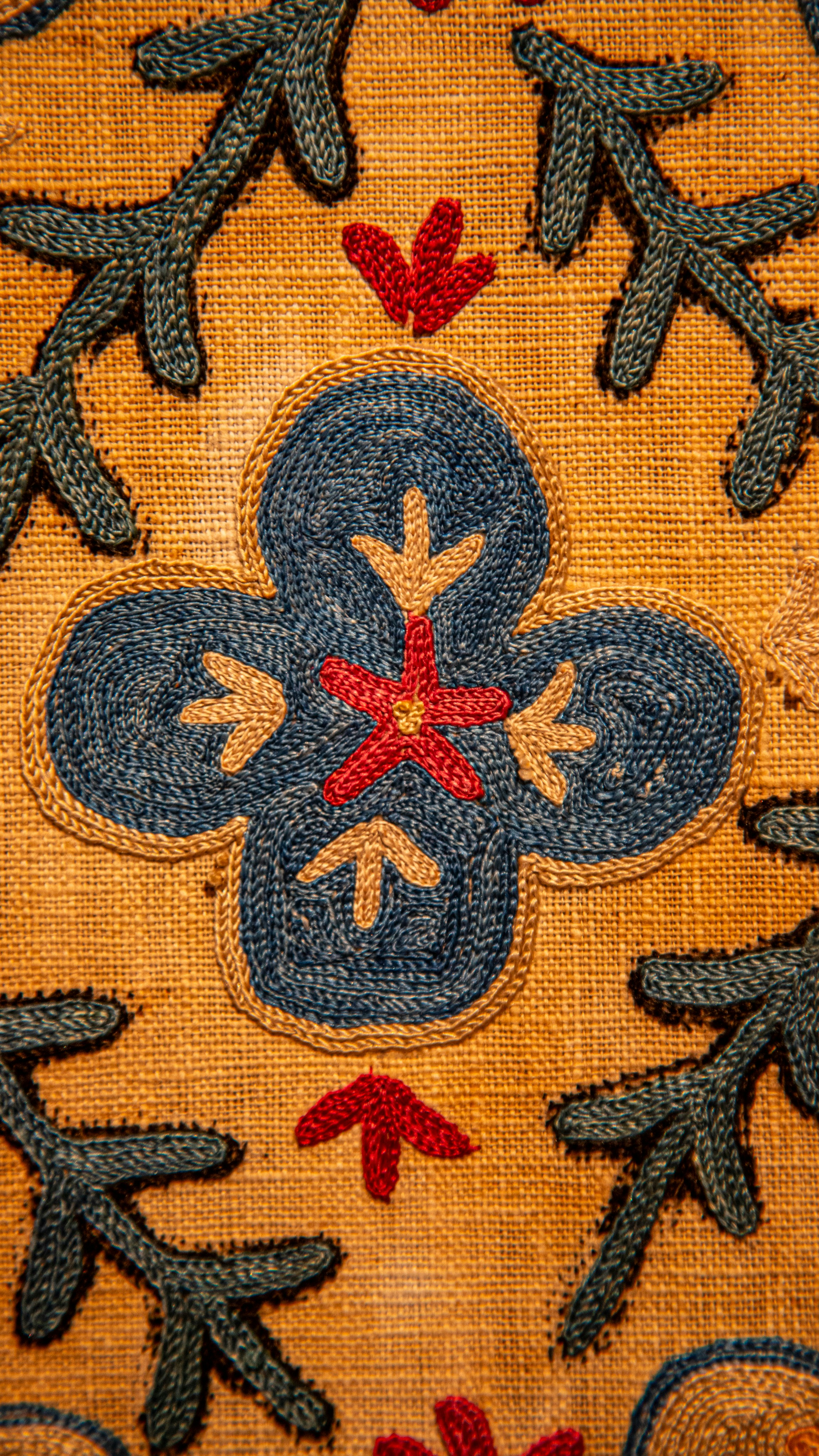 Intricate blue and red floral embroidery on a textured yellow fabric background