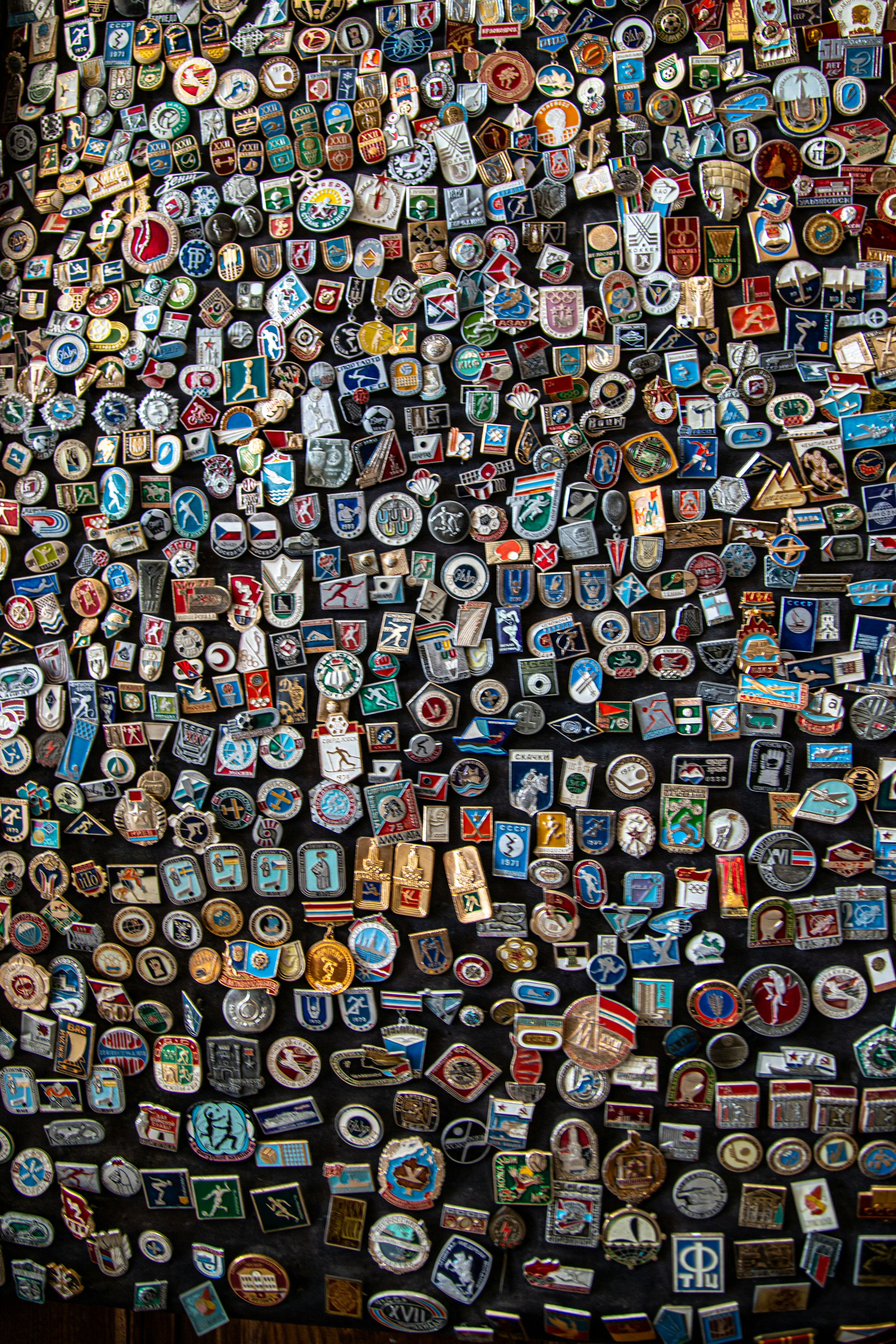 A large collection of vintage metal souvenir pins arranged on a dark fabric background