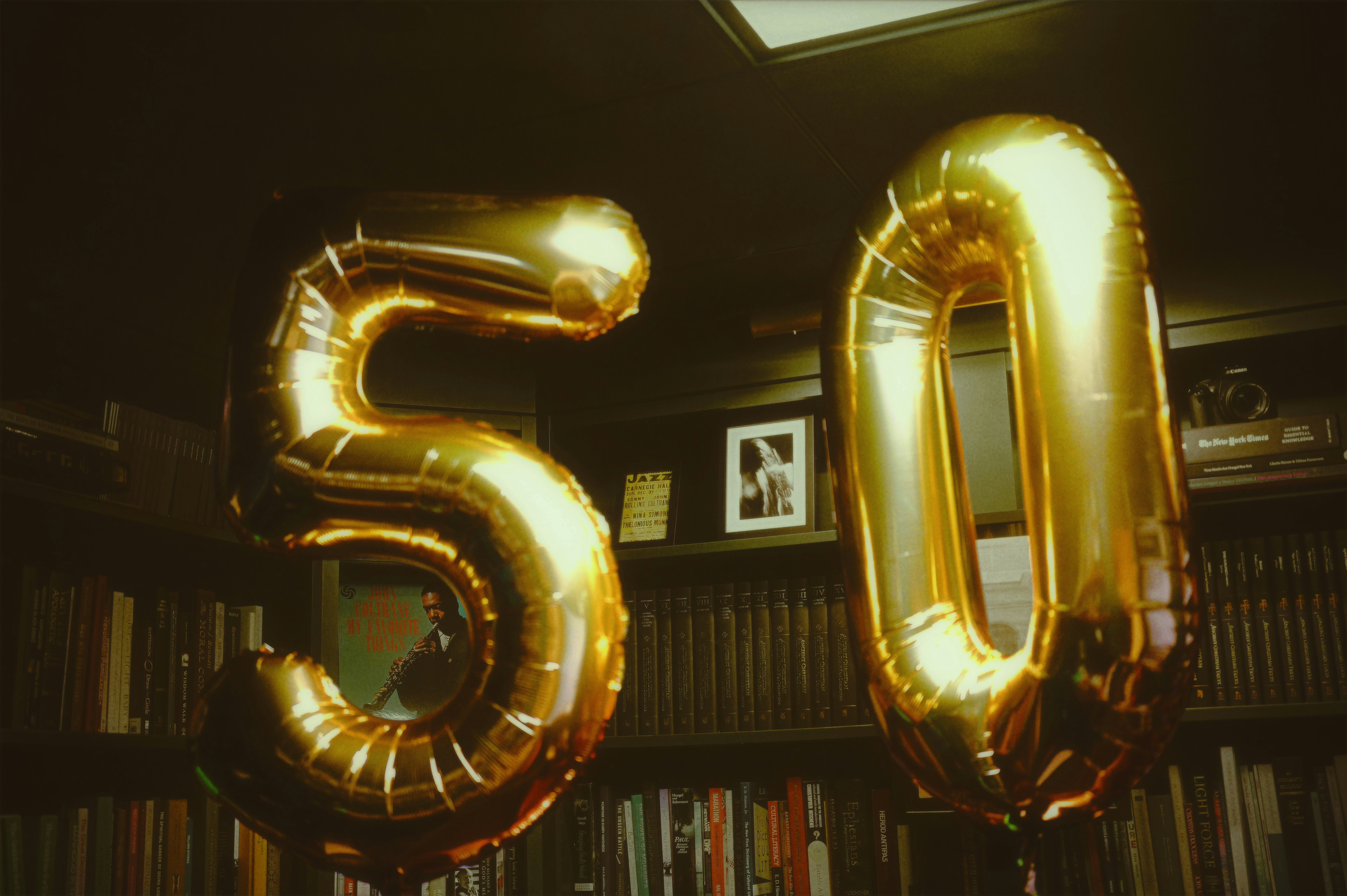 Large gold foil balloons shaped like the number fifty in front of a dark bookshelf