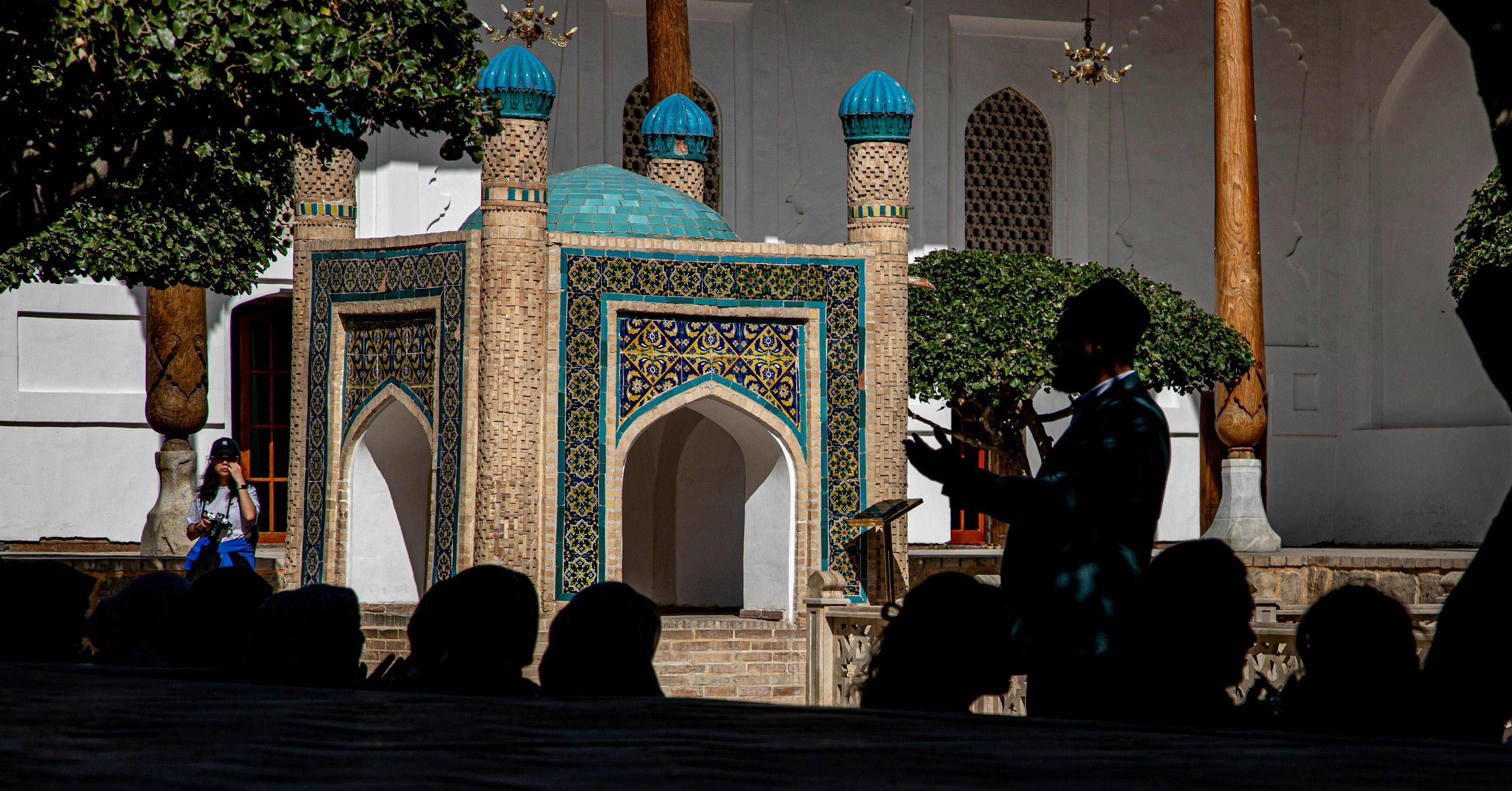 A person gesturing in front of a tiled shrine in a sunlit courtyard