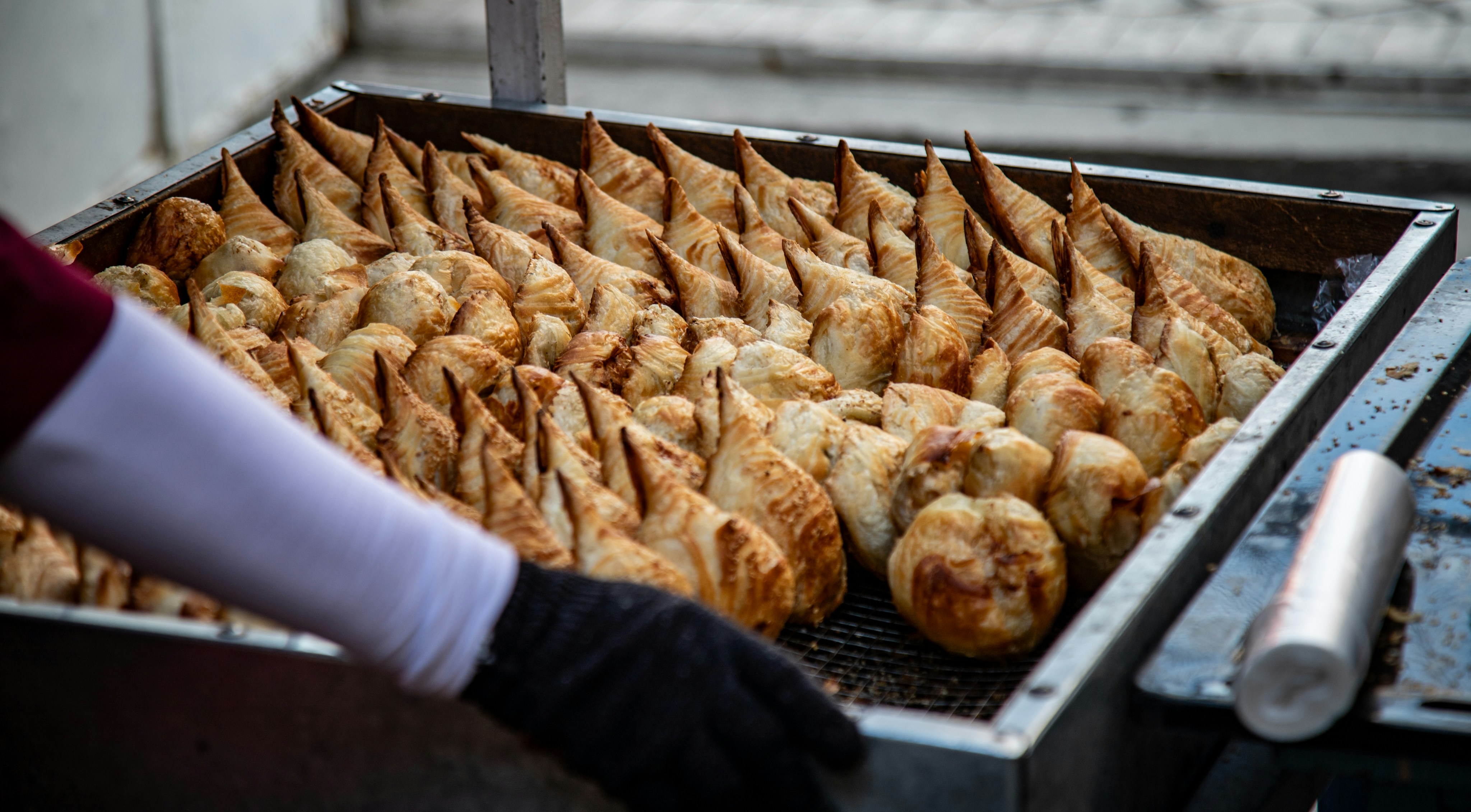 A person in a black glove arranging rows of golden brown pastries on a metal tray