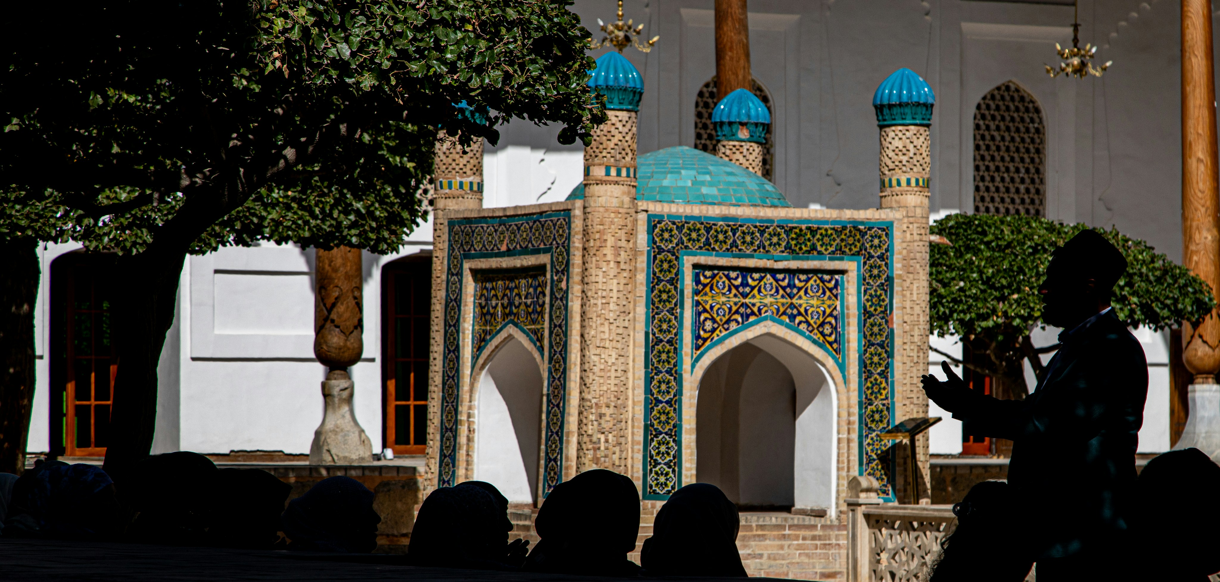 A person in silhouette praying before a tiled shrine in a sunlit courtyard