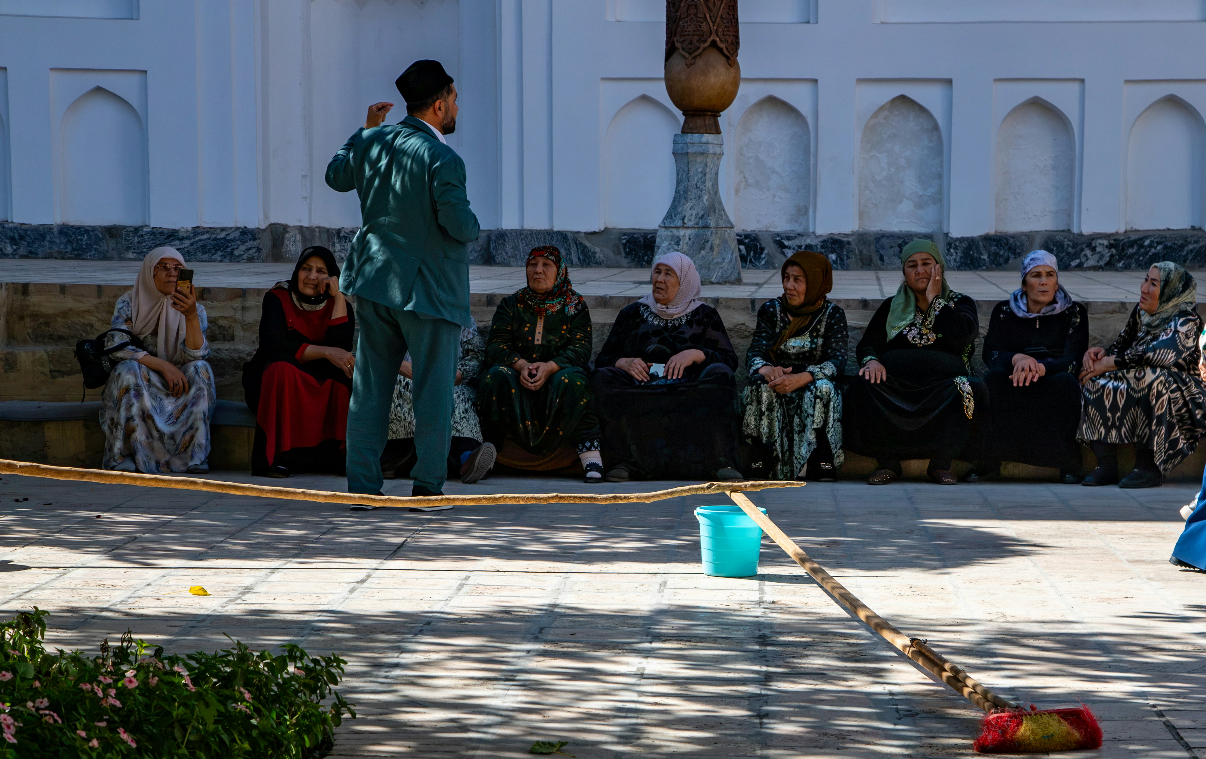 A man in a suit gesturing to a group of women sitting on a stone ledge