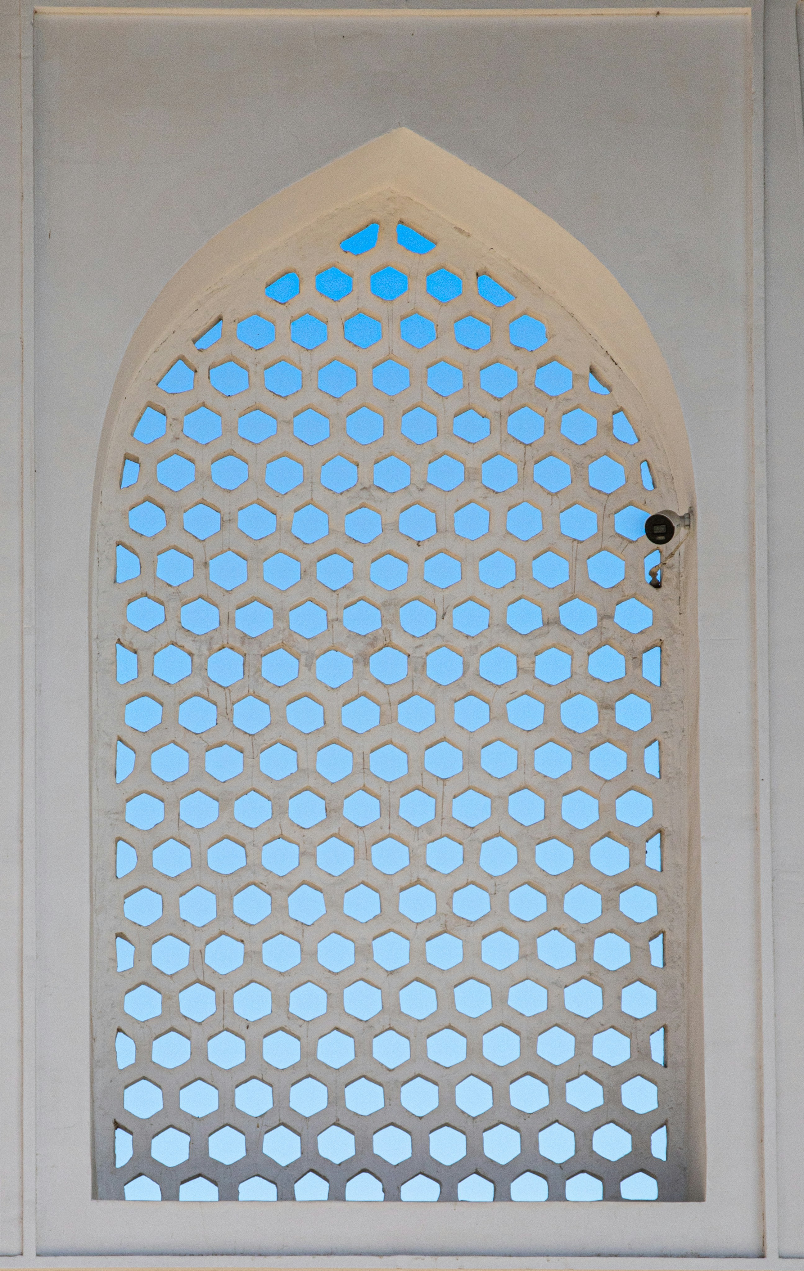 A white arched screen with a hexagonal lattice pattern against a clear blue sky