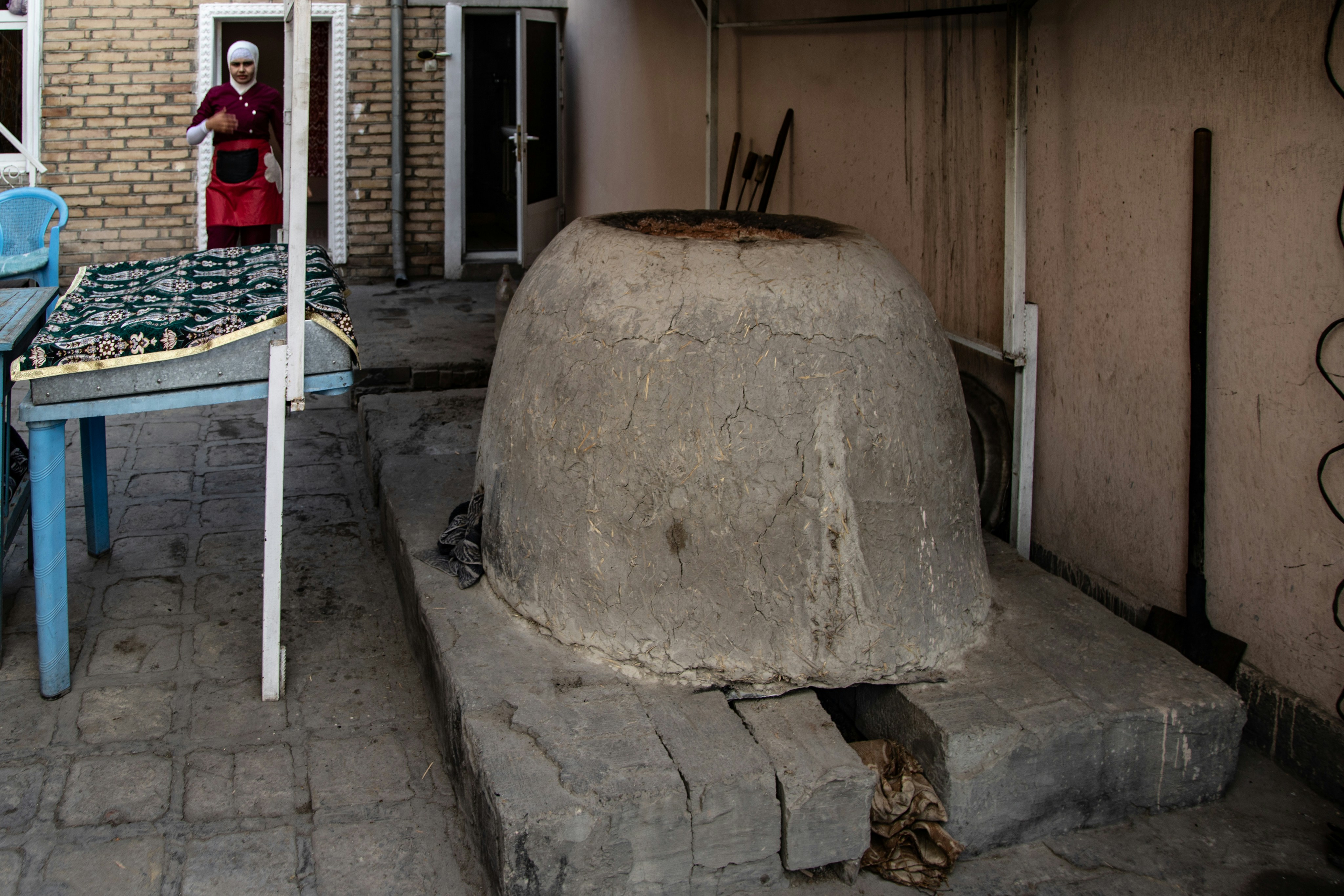A large clay tandoor oven in a courtyard with a person in the background