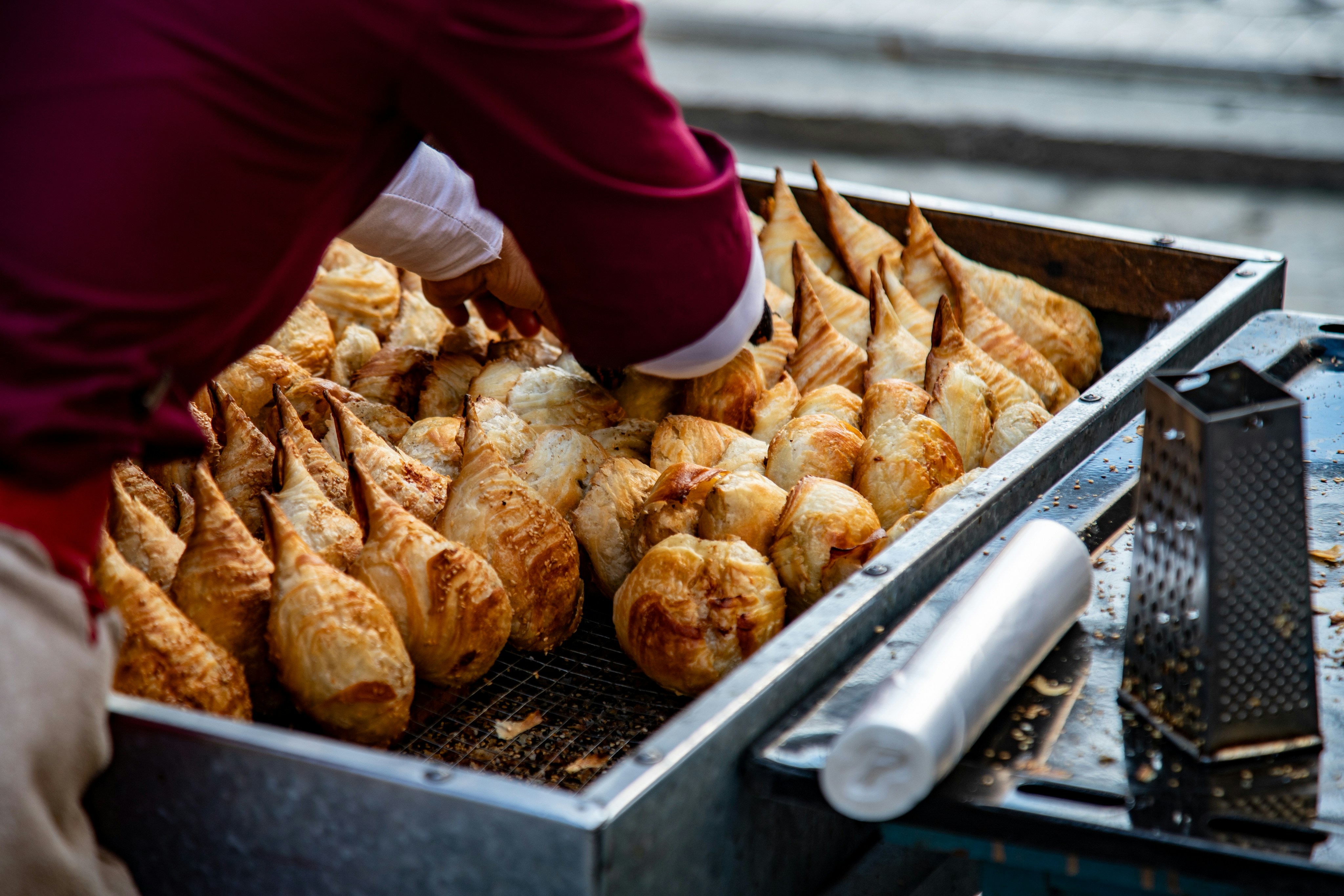 A person in a maroon shirt arranging golden brown pastries on a metal tray