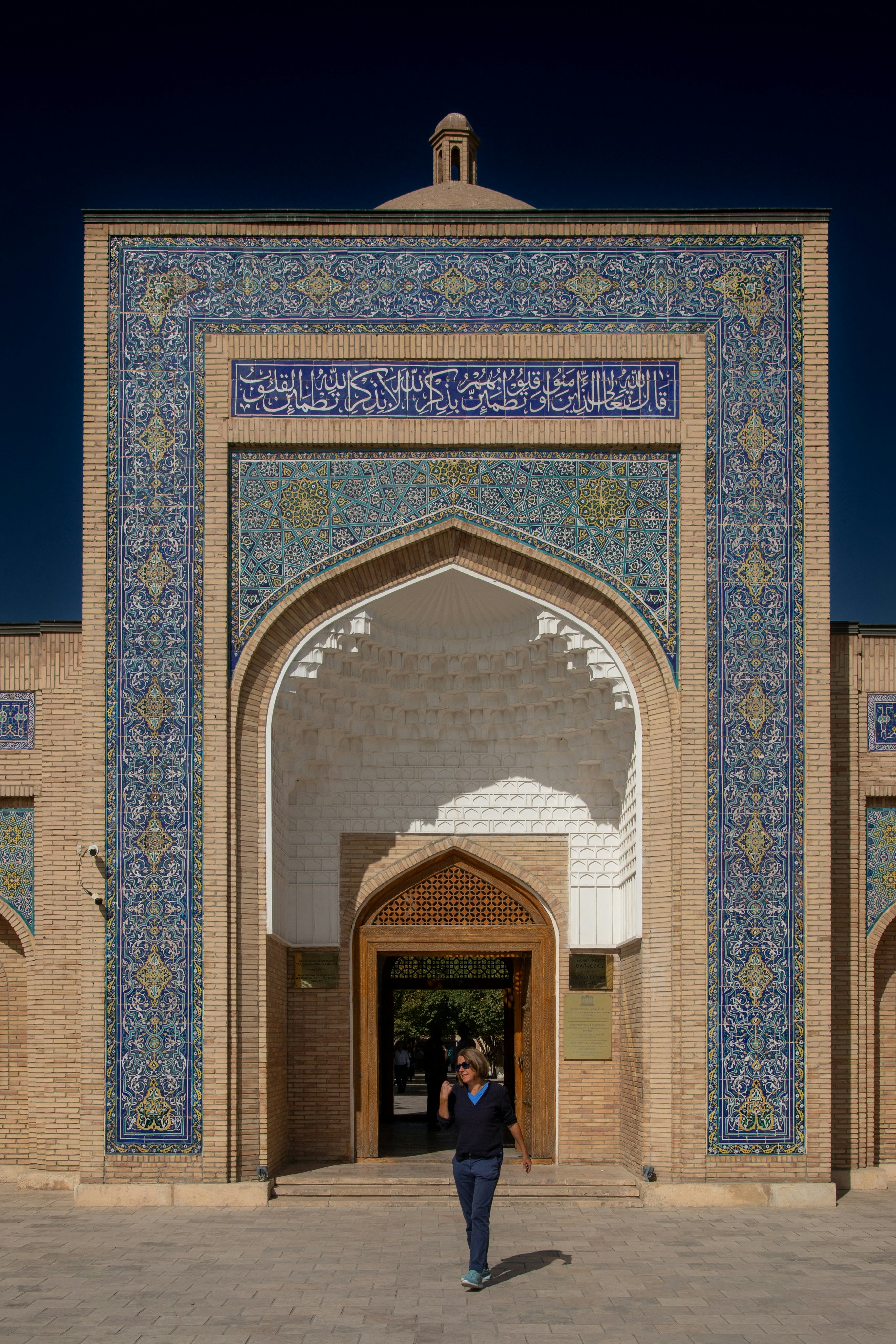 A person walking from the arched entrance of a tiled brick building in Bukhara
