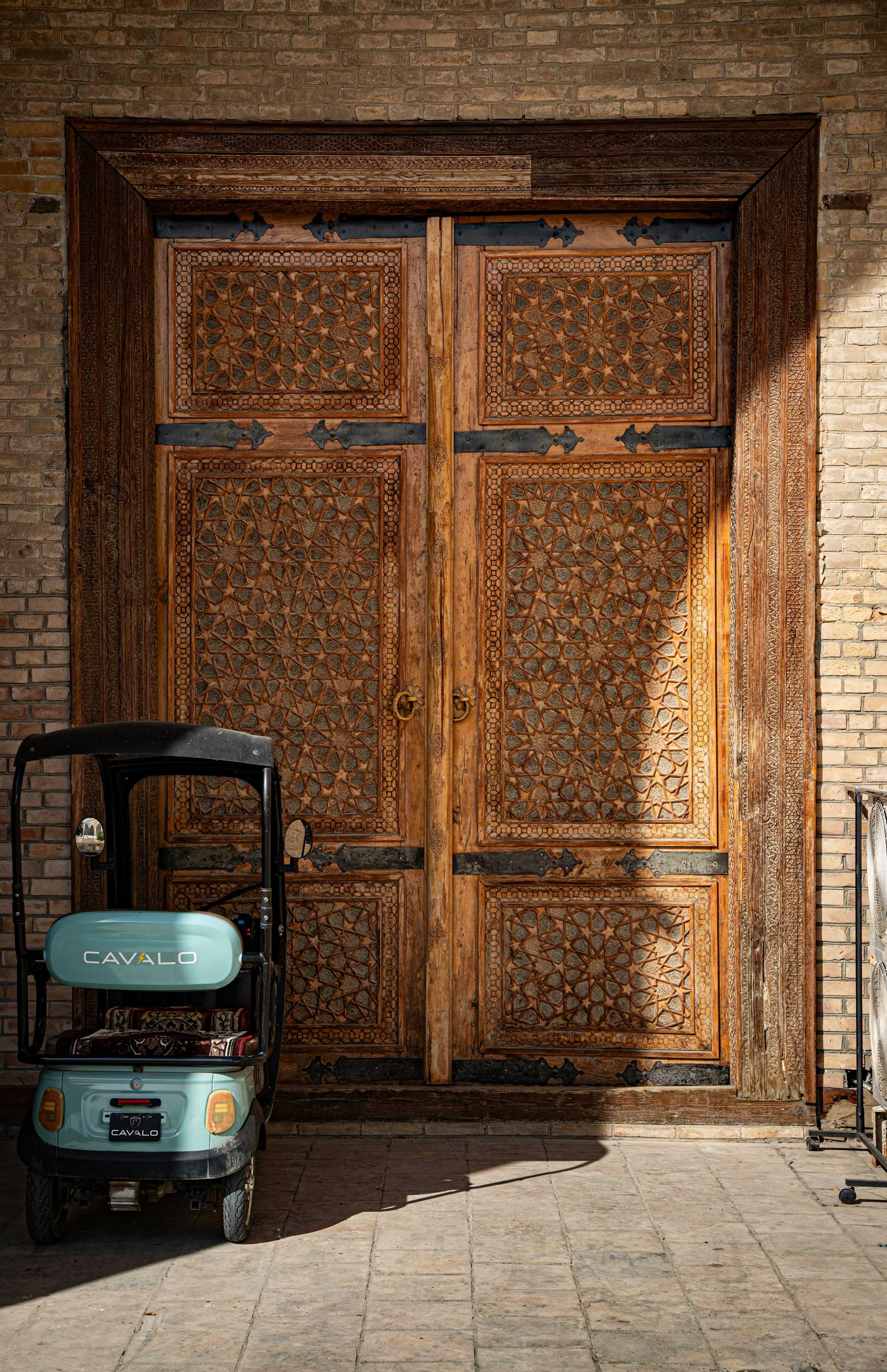 A light blue electric mobility scooter parked before a large wooden door with intricate geometric carvings