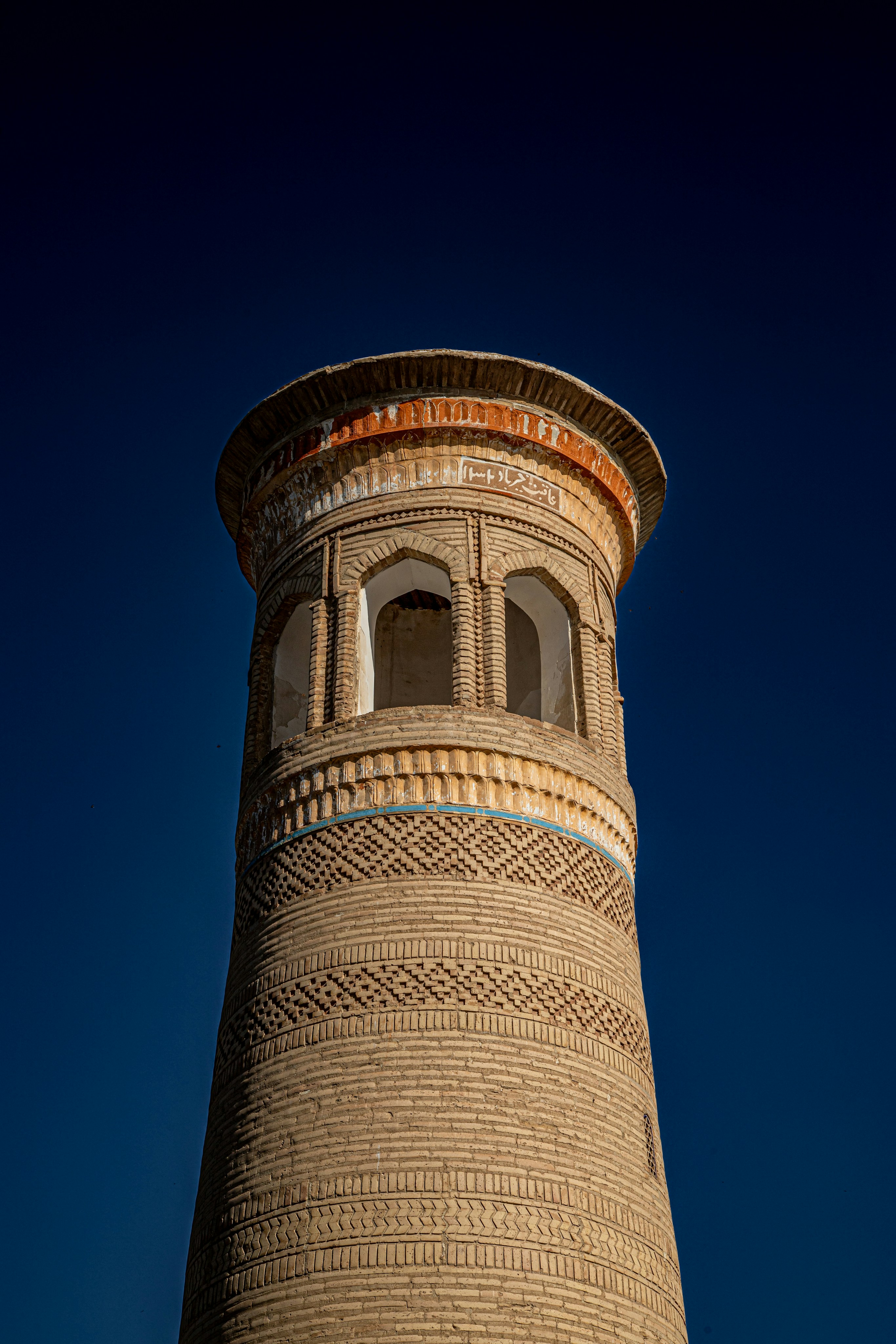 A tall cylindrical brick minaret with arched openings against a deep blue sky