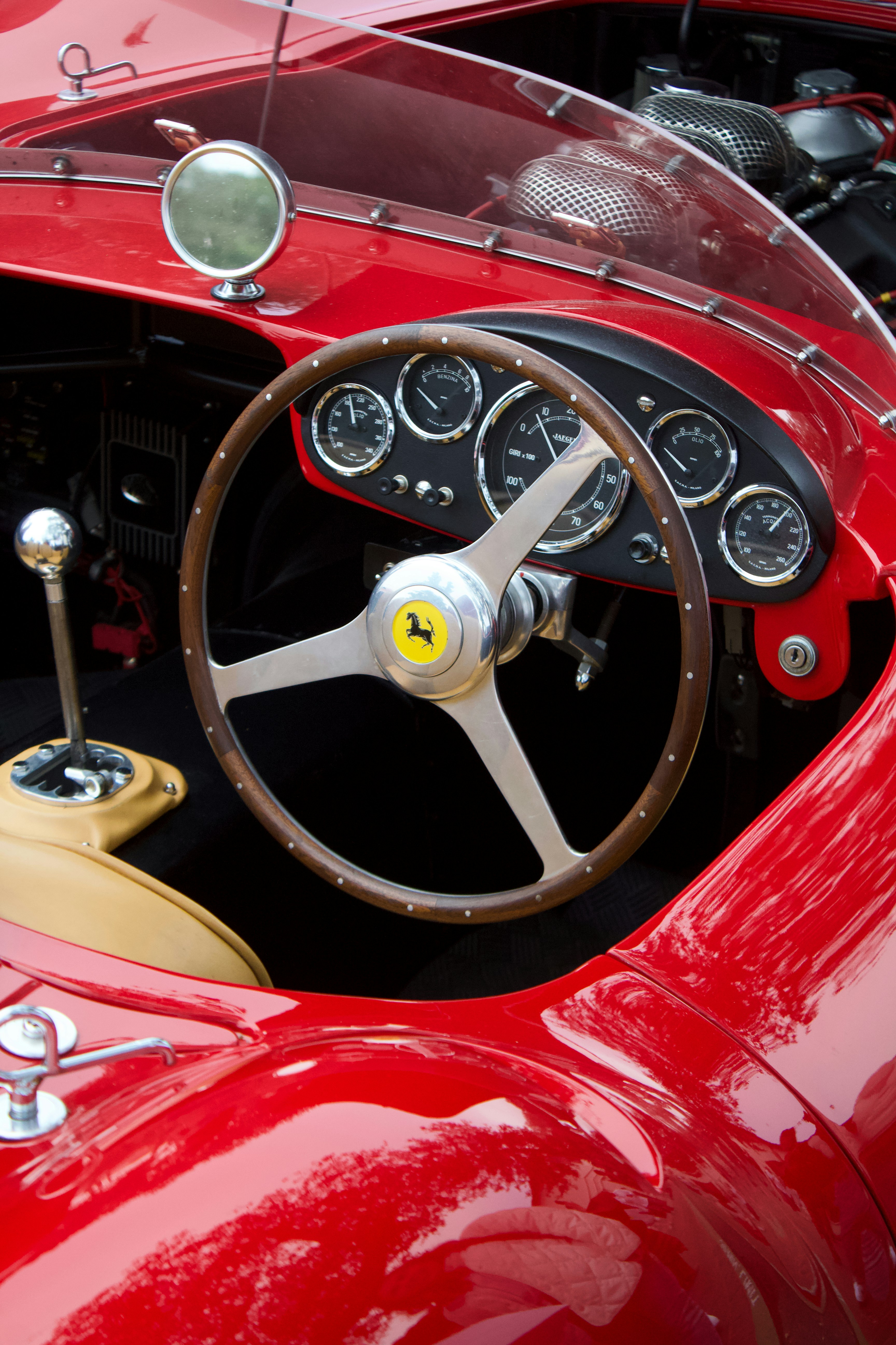 The interior of a vintage red Ferrari sports car with a wooden steering wheel and analog gauges