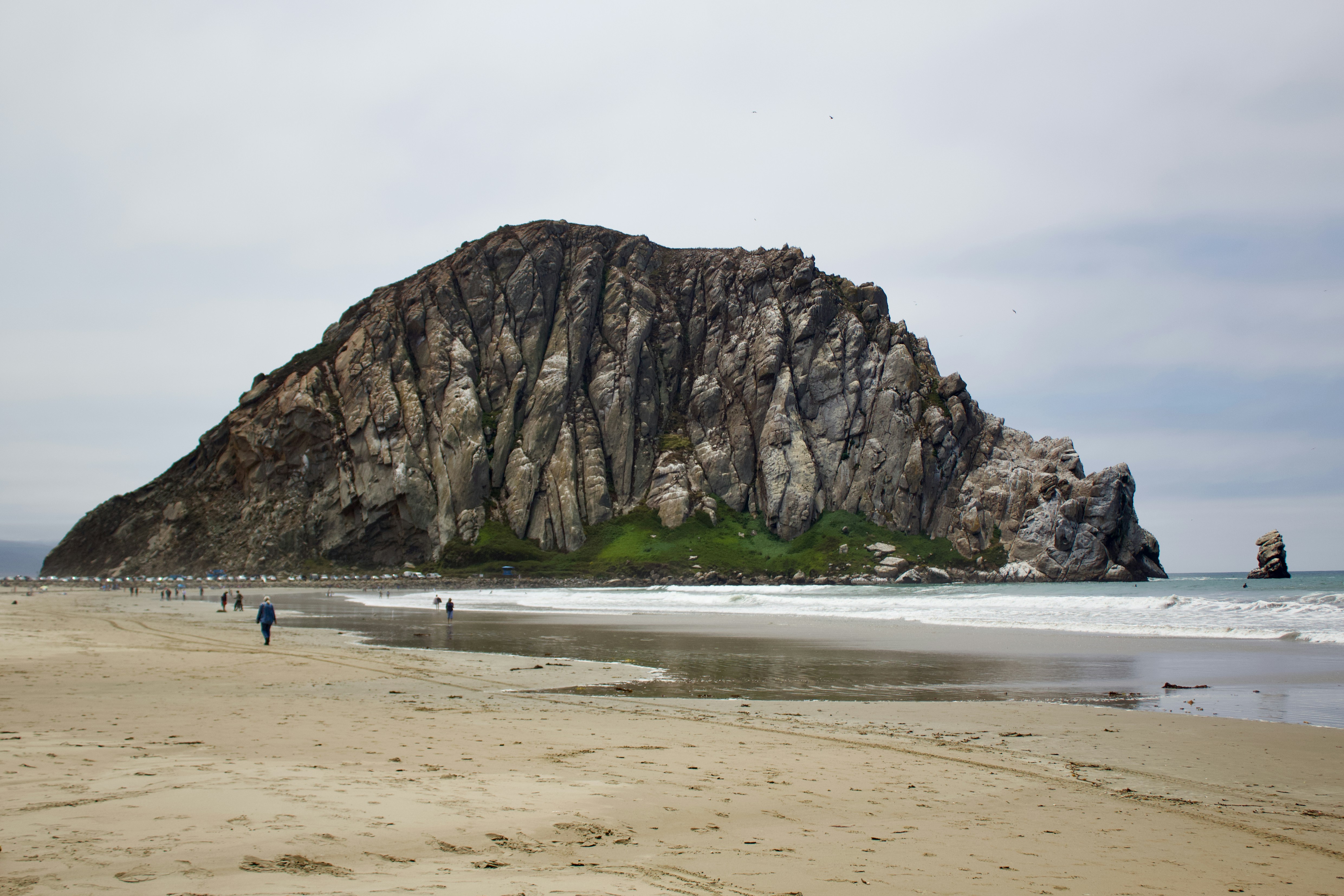 Morro Rock rising above a sandy beach with gentle waves under a cloudy sky