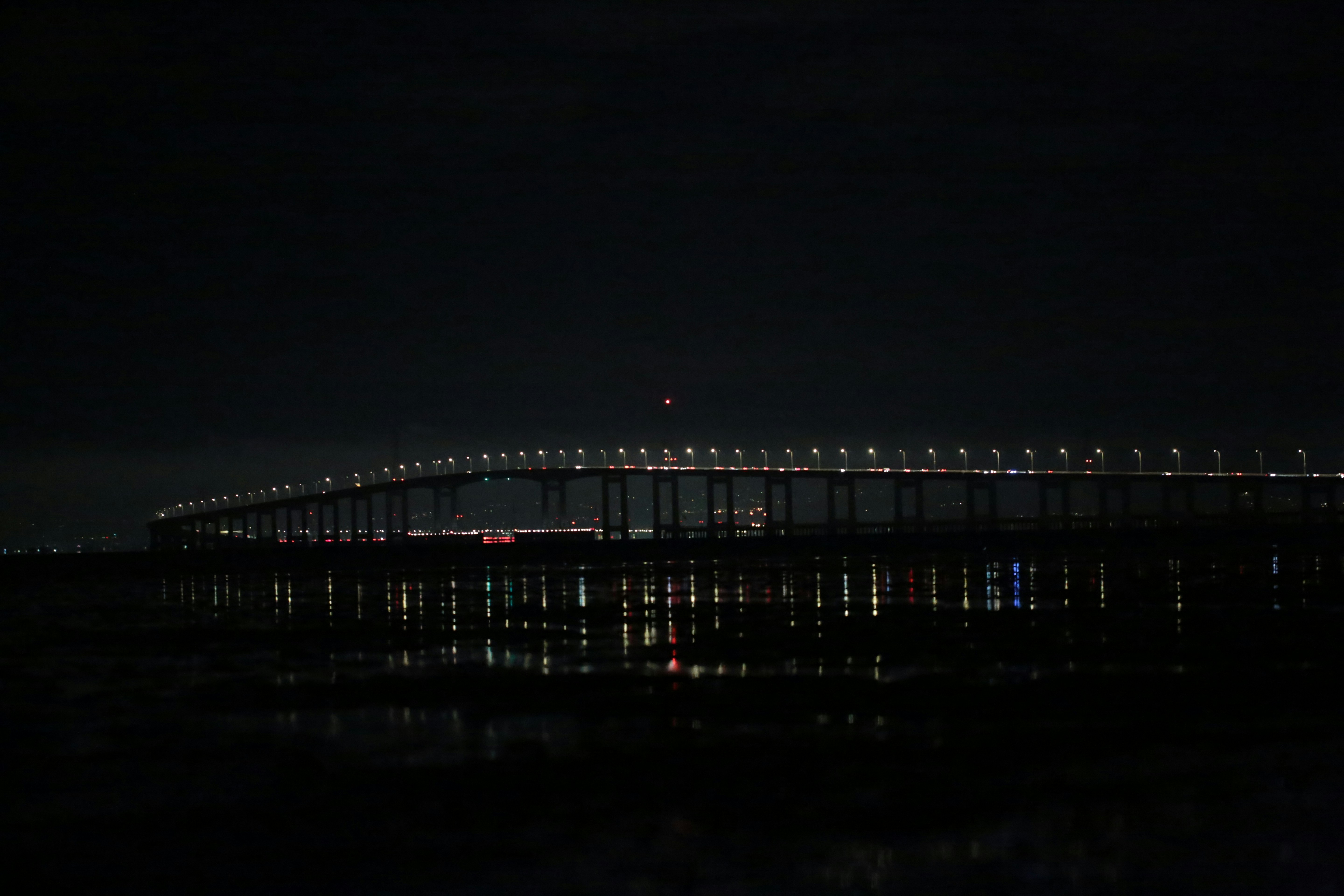 A long bridge illuminated by streetlights at night reflecting on dark water