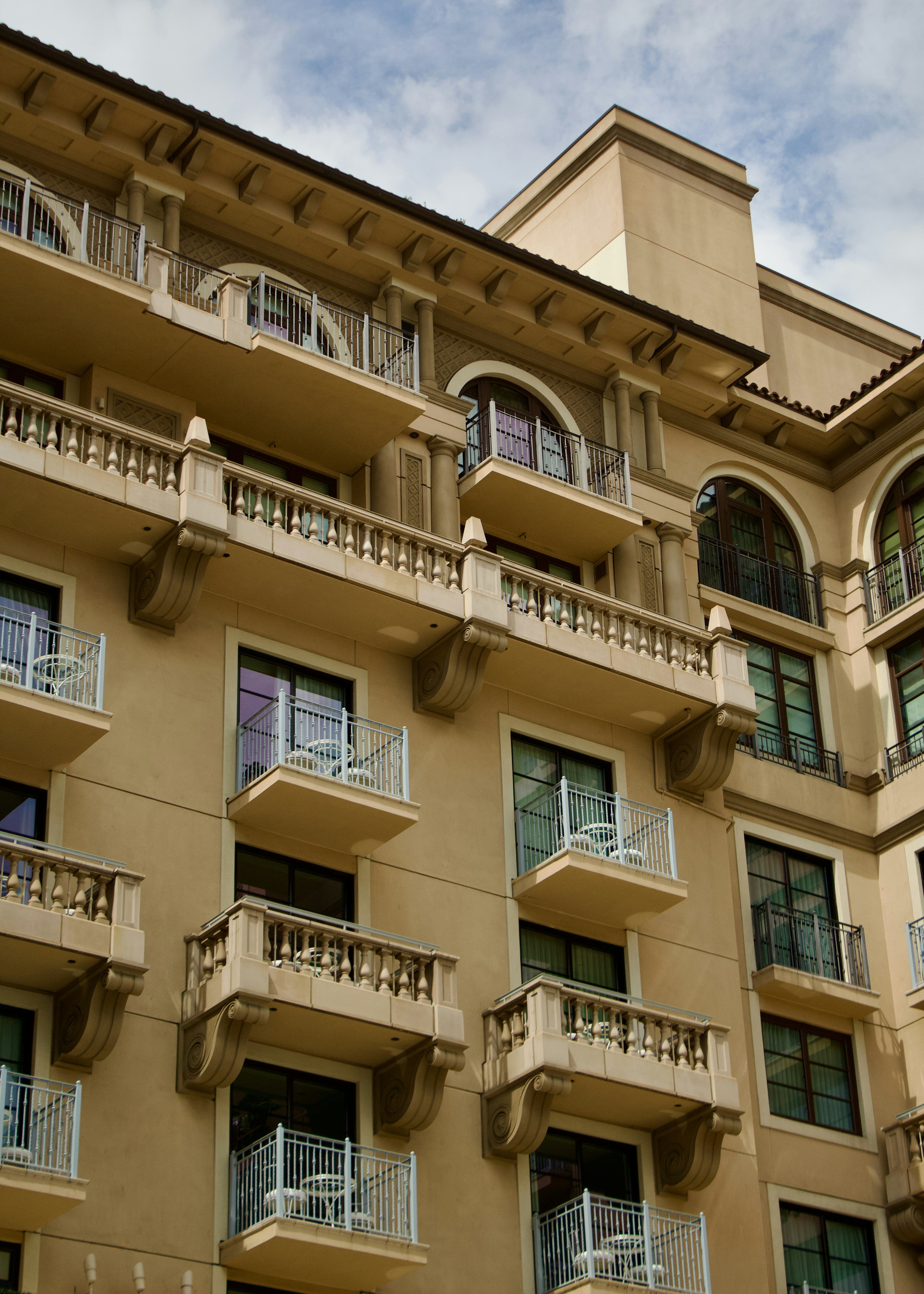 A beige hotel building with multiple balconies and arched windows under a cloudy sky