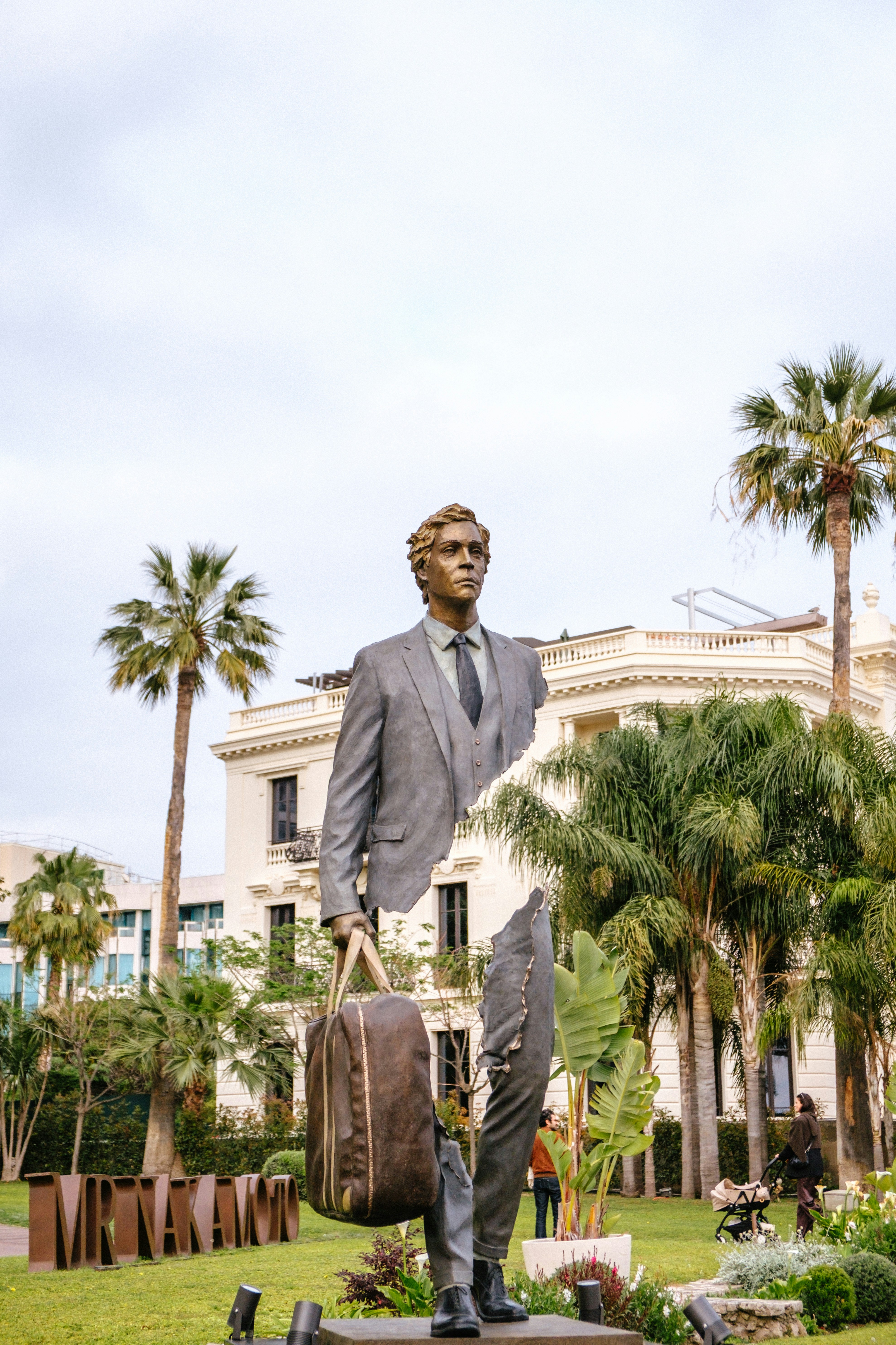 A bronze sculpture of a man in a suit carrying a bag in a park
