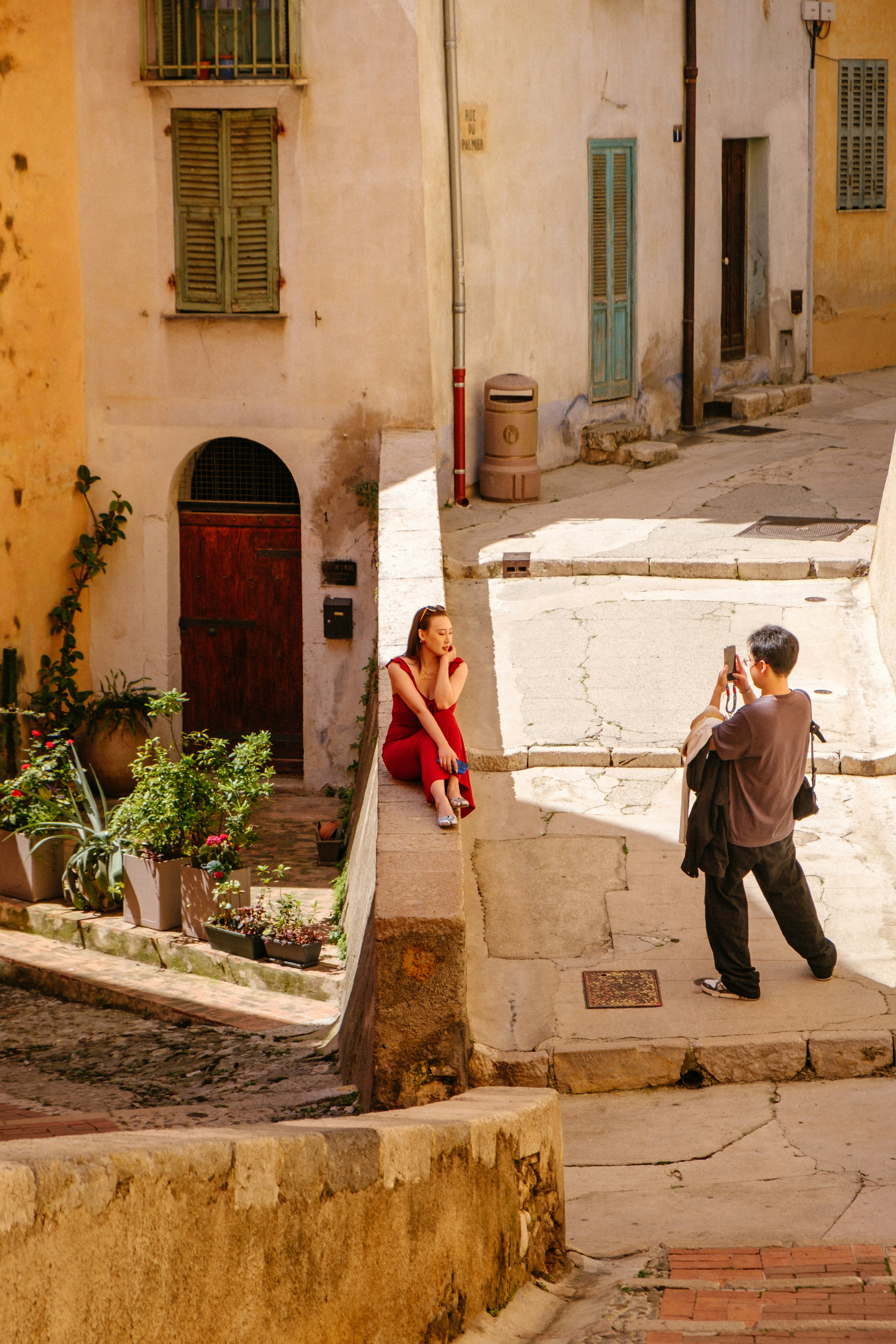 A woman in a red jumpsuit posing on a stone wall as a man photographs her