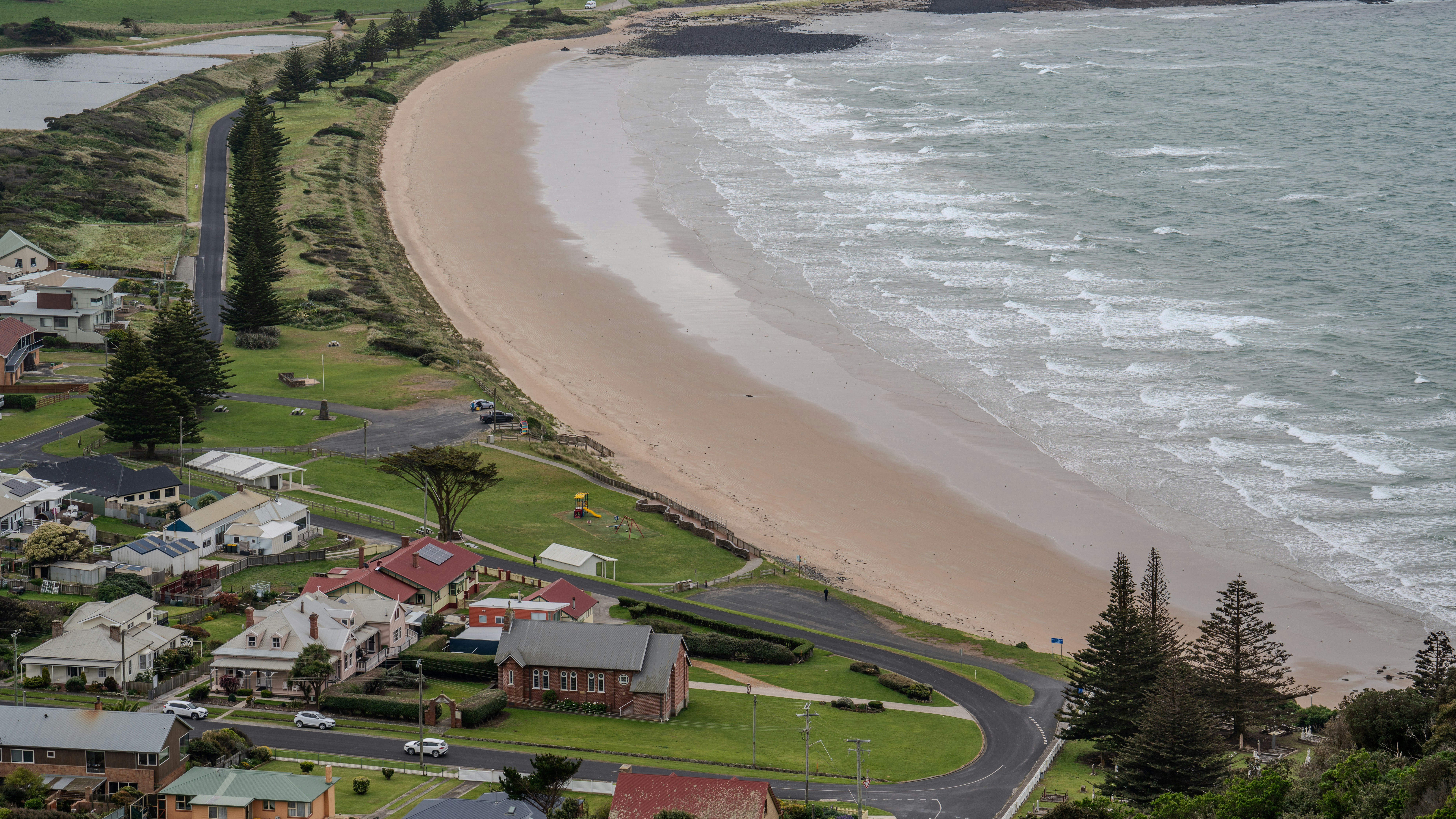 An aerial view of a coastal town with houses along a sandy beach and ocean waves
