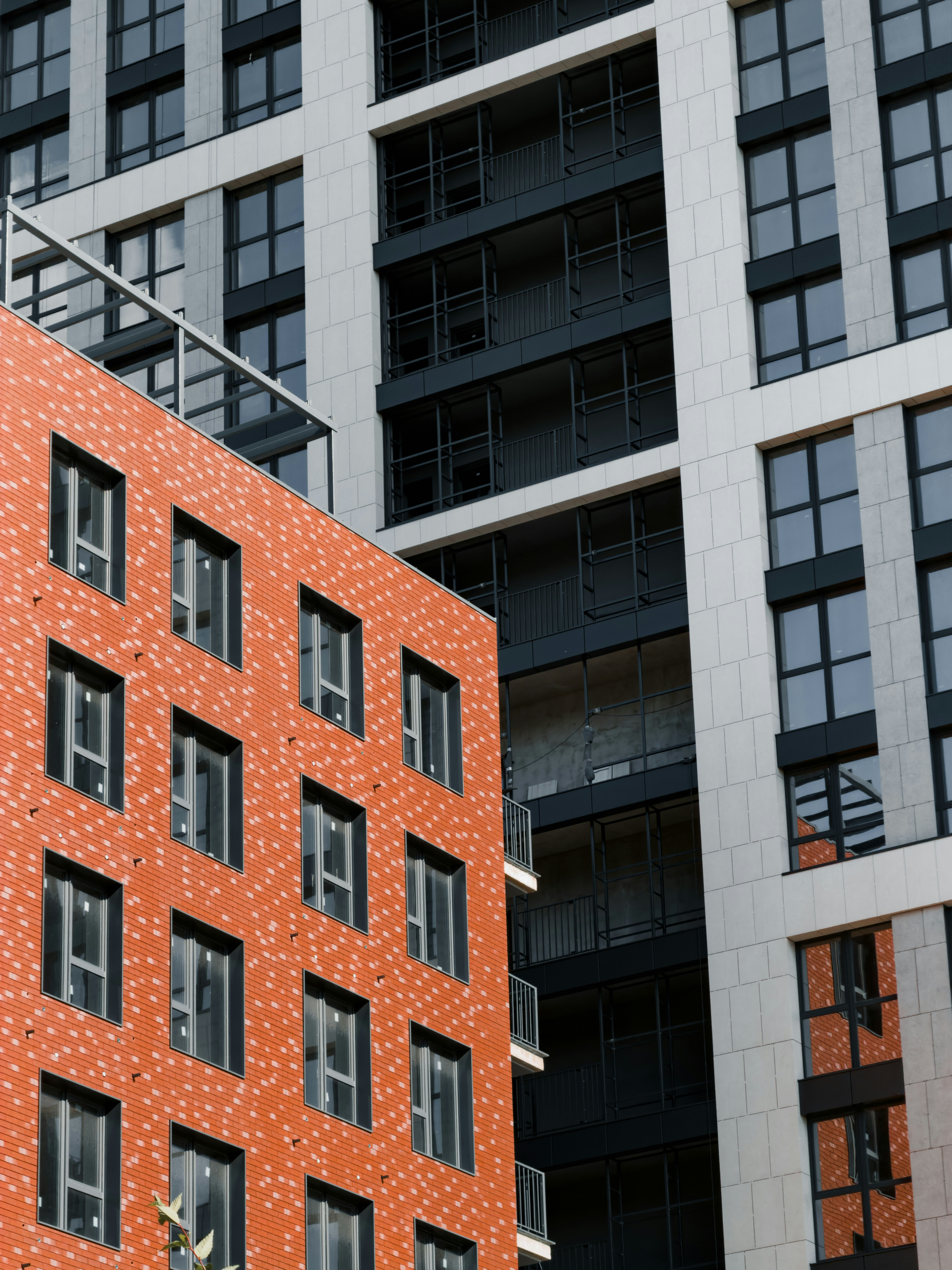 A modern orange brick building facade beside a white and black high-rise apartment complex