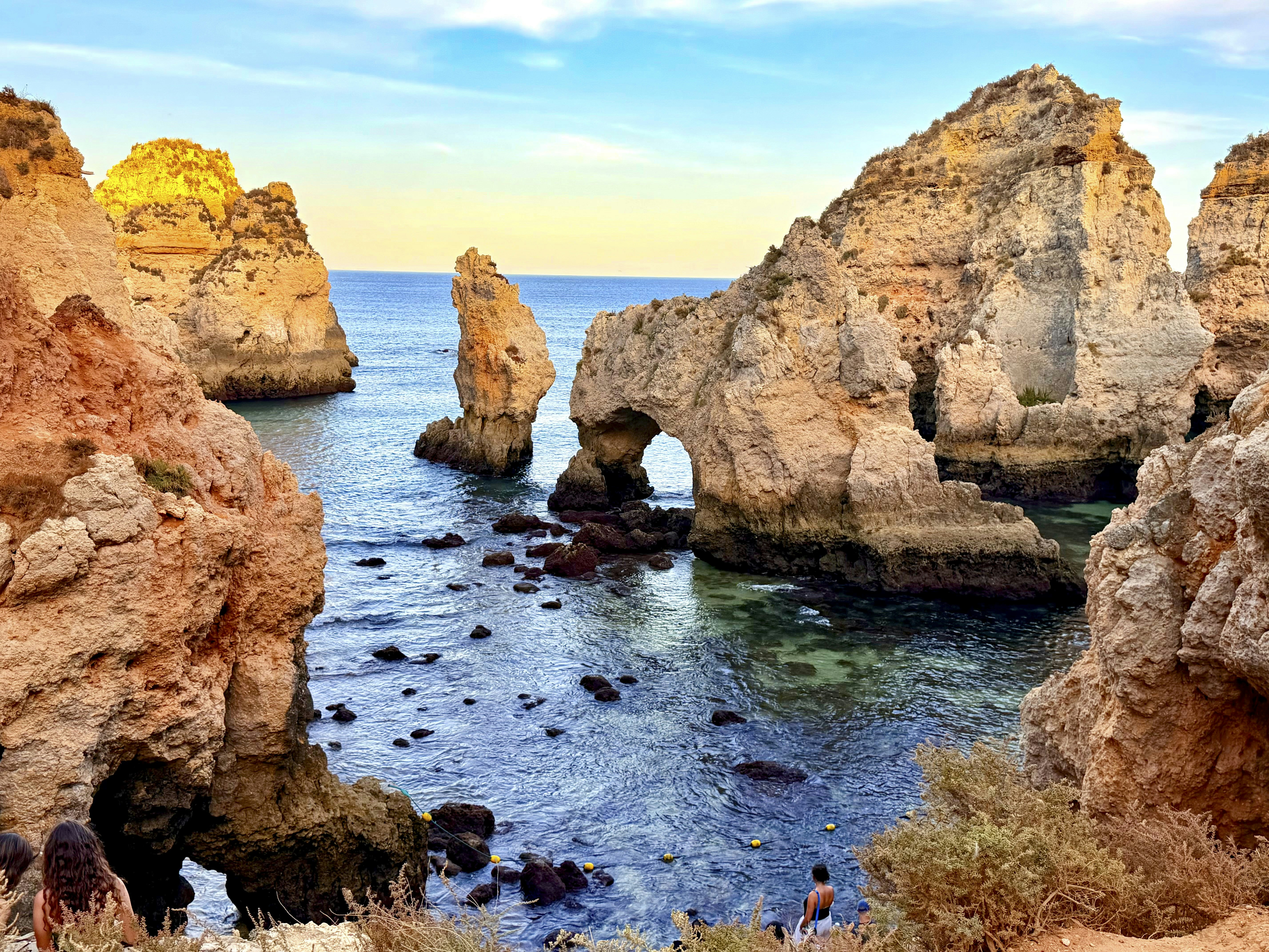 People looking at limestone sea stacks and a natural arch in the Algarve, Portugal