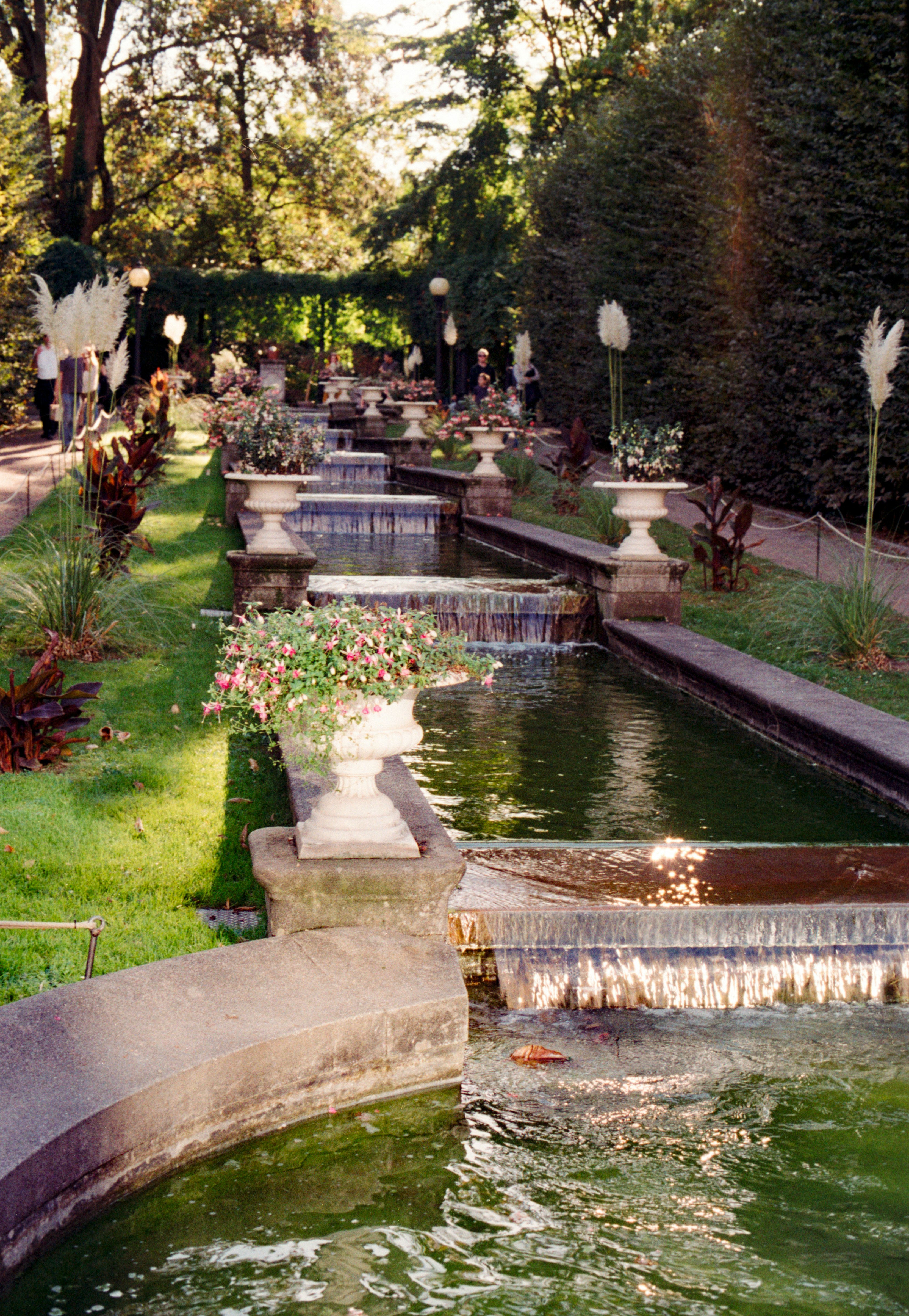 Ein gestuftes Wasserspiel mit Steinbecken und Blumentöpfen in einem üppigen Garten