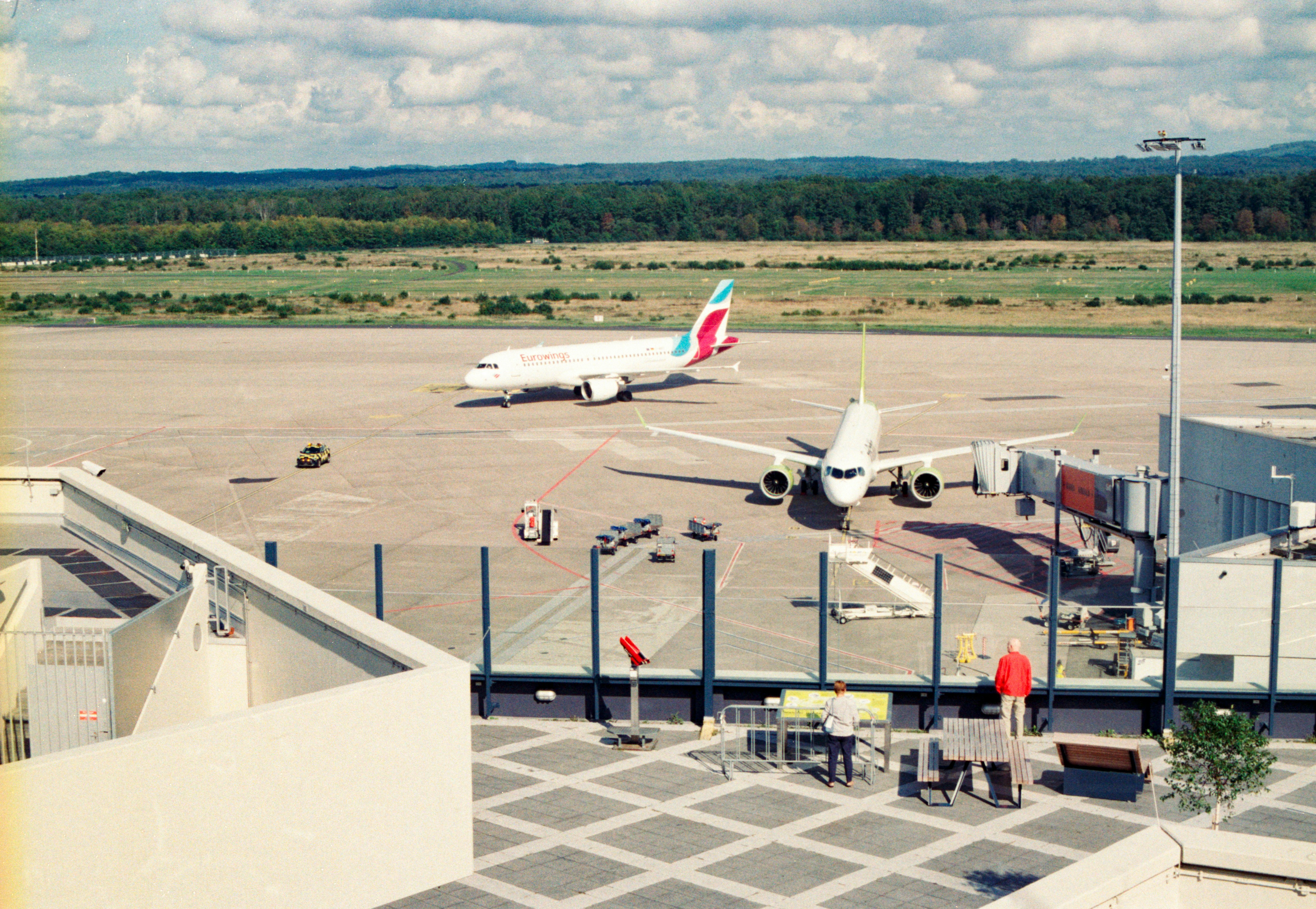 Zwei Flugzeuge auf einem Flughafen-Rollfeld mit Zuschauern von einer Aussichtsplattform aus