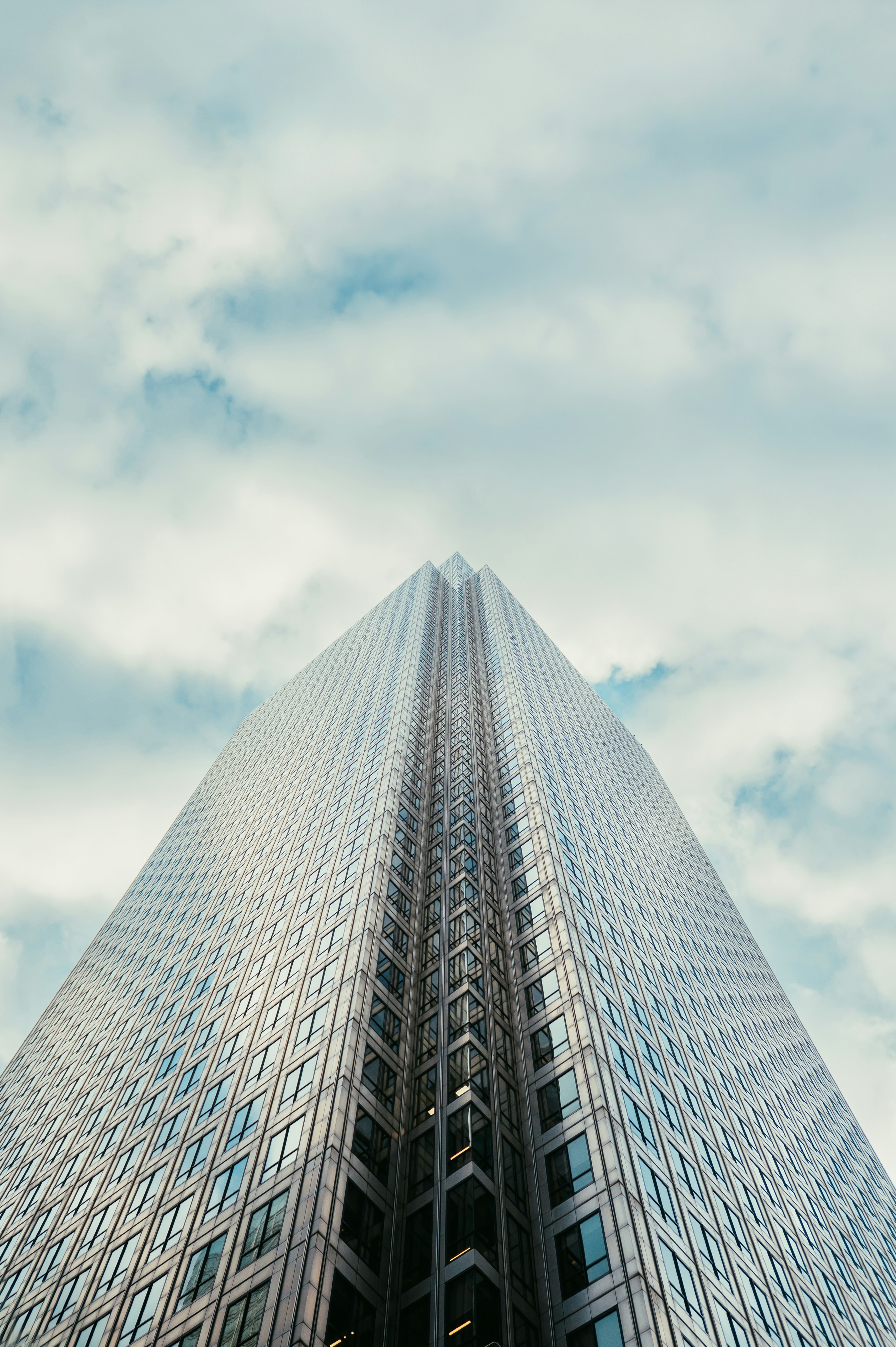 A low angle view of a modern glass skyscraper against a cloudy blue sky