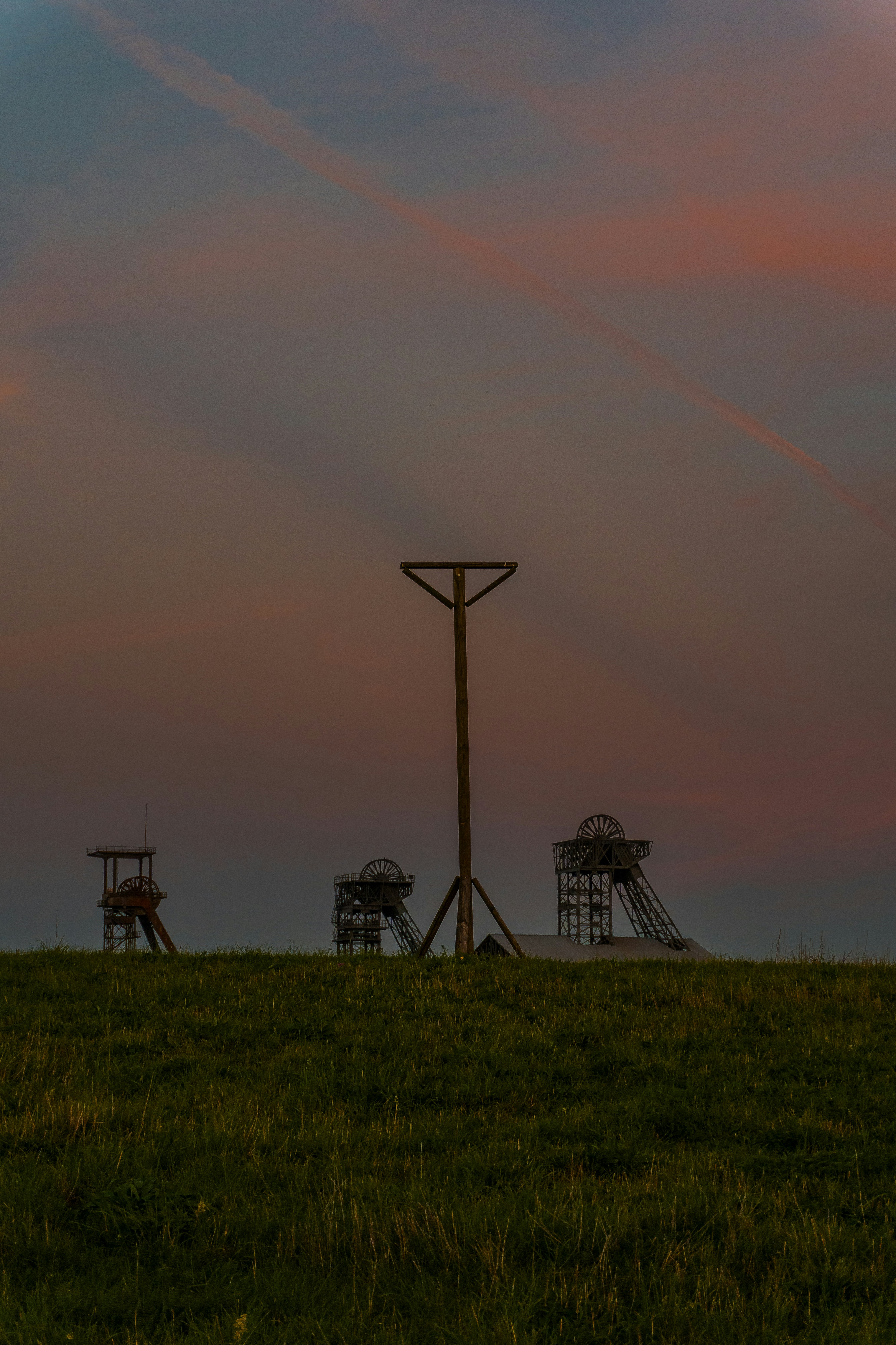Silhouetted mine headframes and a tall wooden pole against a warm orange sky