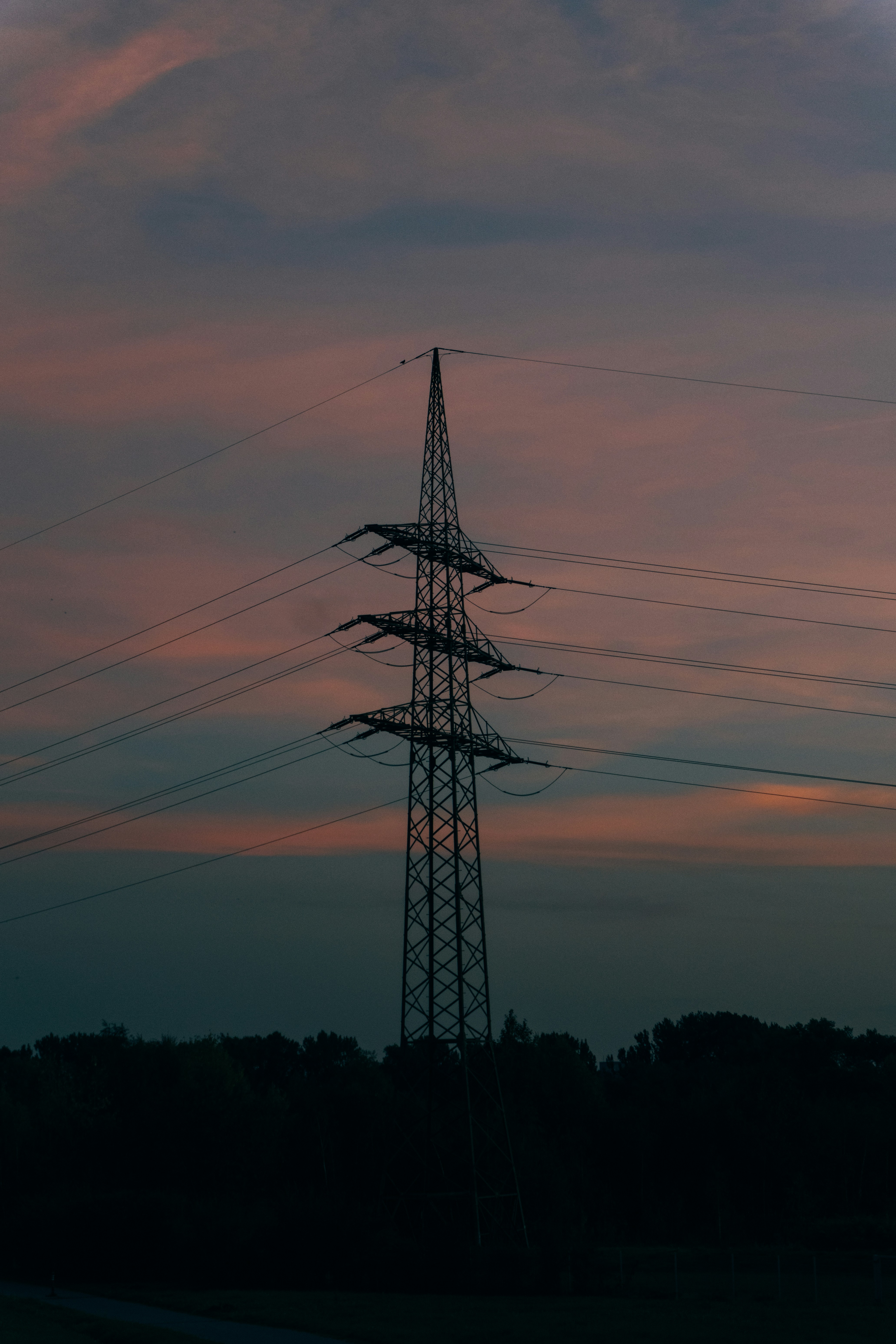 A tall electricity pylon in silhouette against a warm orange and dark blue sky